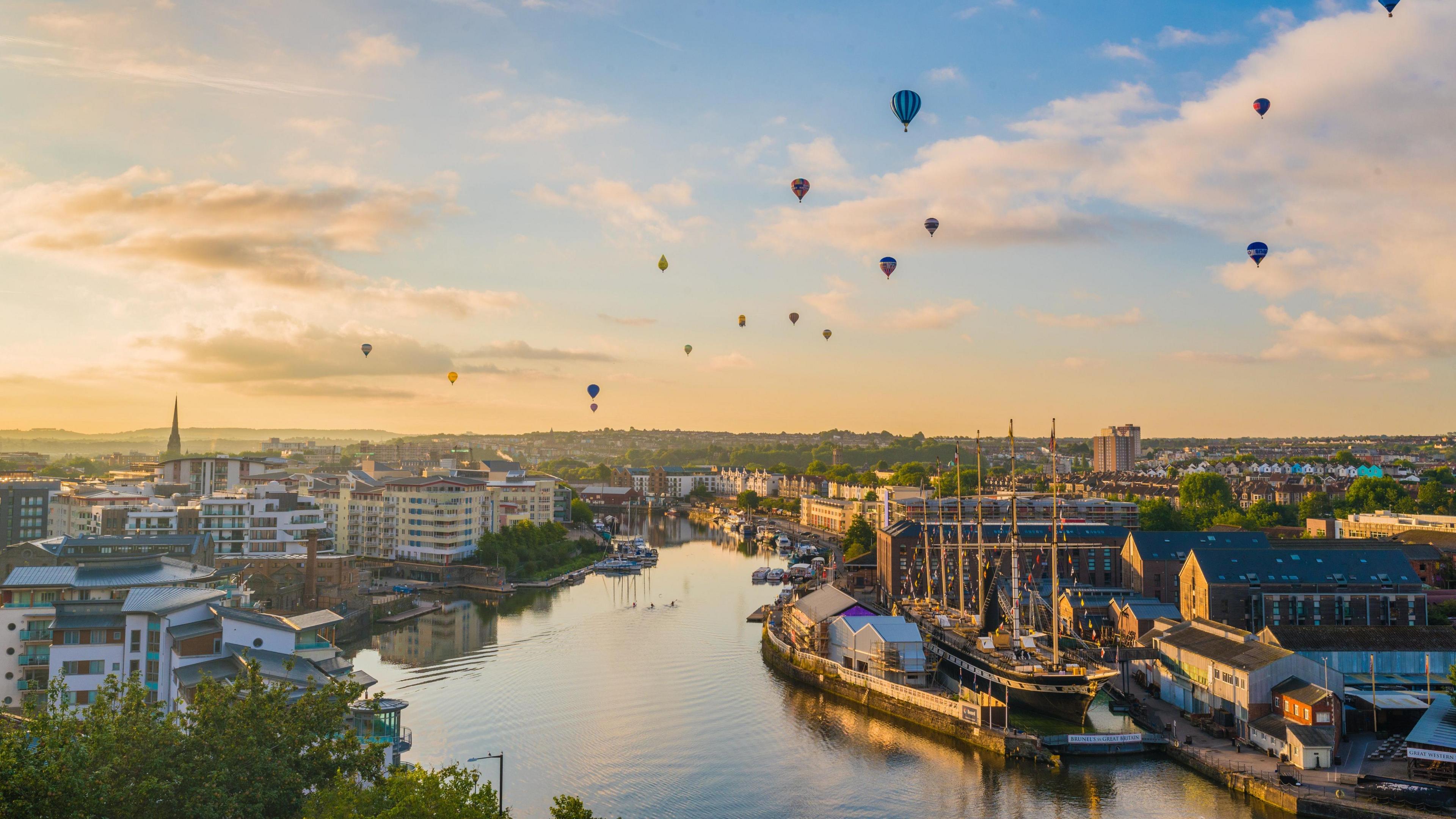 Bristol's Harbourside pictured from above at sunrise or sunset with dozens of balloons floating above the city skyline. 