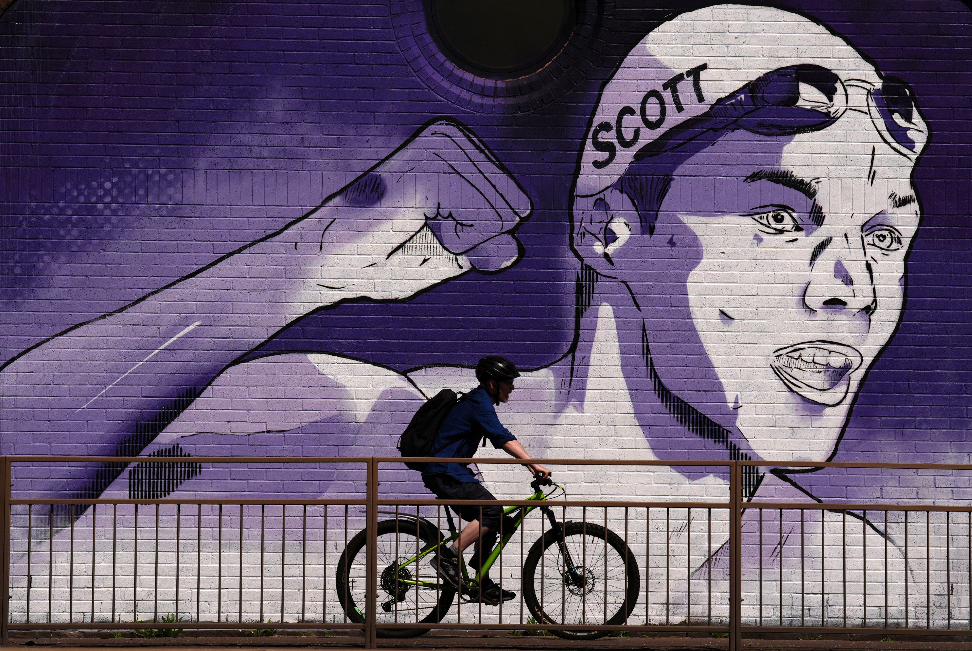 A man cycles pas a large mural of swimmer Duncan Scott