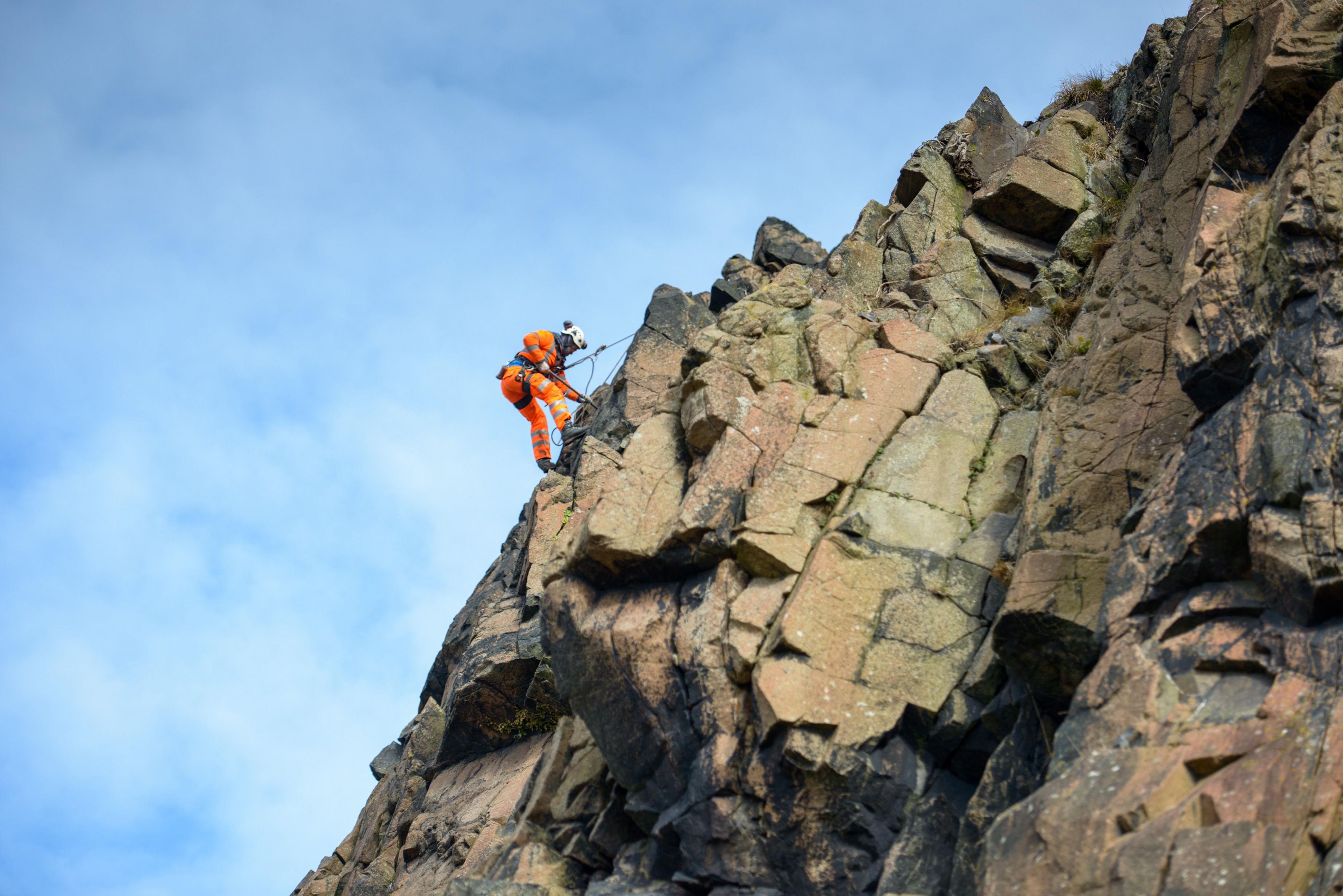 Man in orange suit attached to a cliff from a rope.