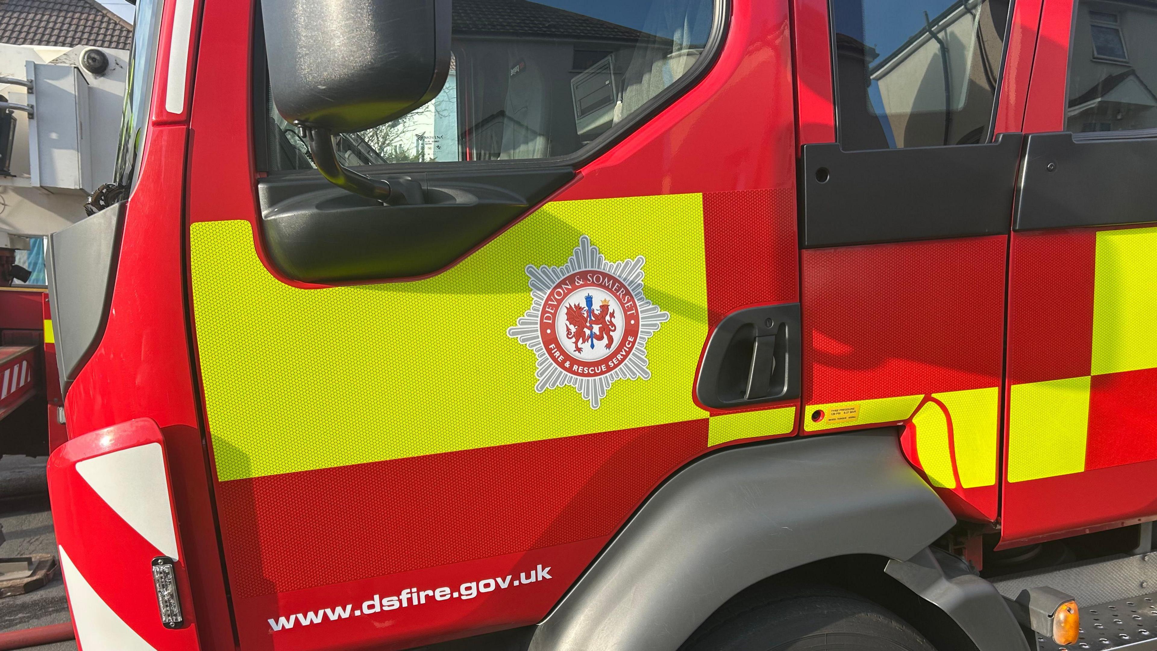 Close up shot of a Devon and Somerset Fire Service engine at the scene of an incident. The vehicle is red and yellow and has the service's emblem on the door.