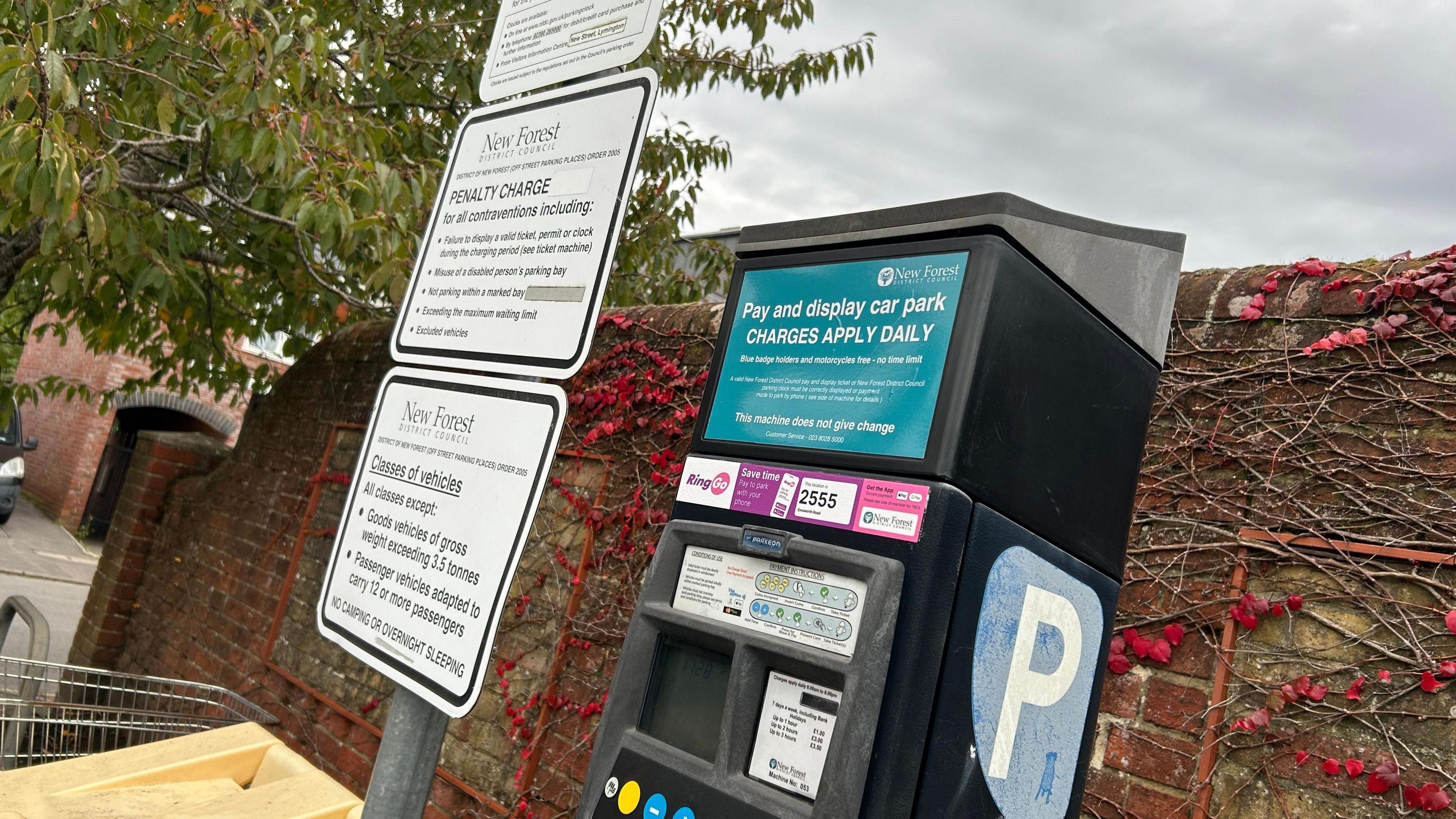 A New Forest District Council car park ticket machine in front of a brick wall with white regulations signs to its left