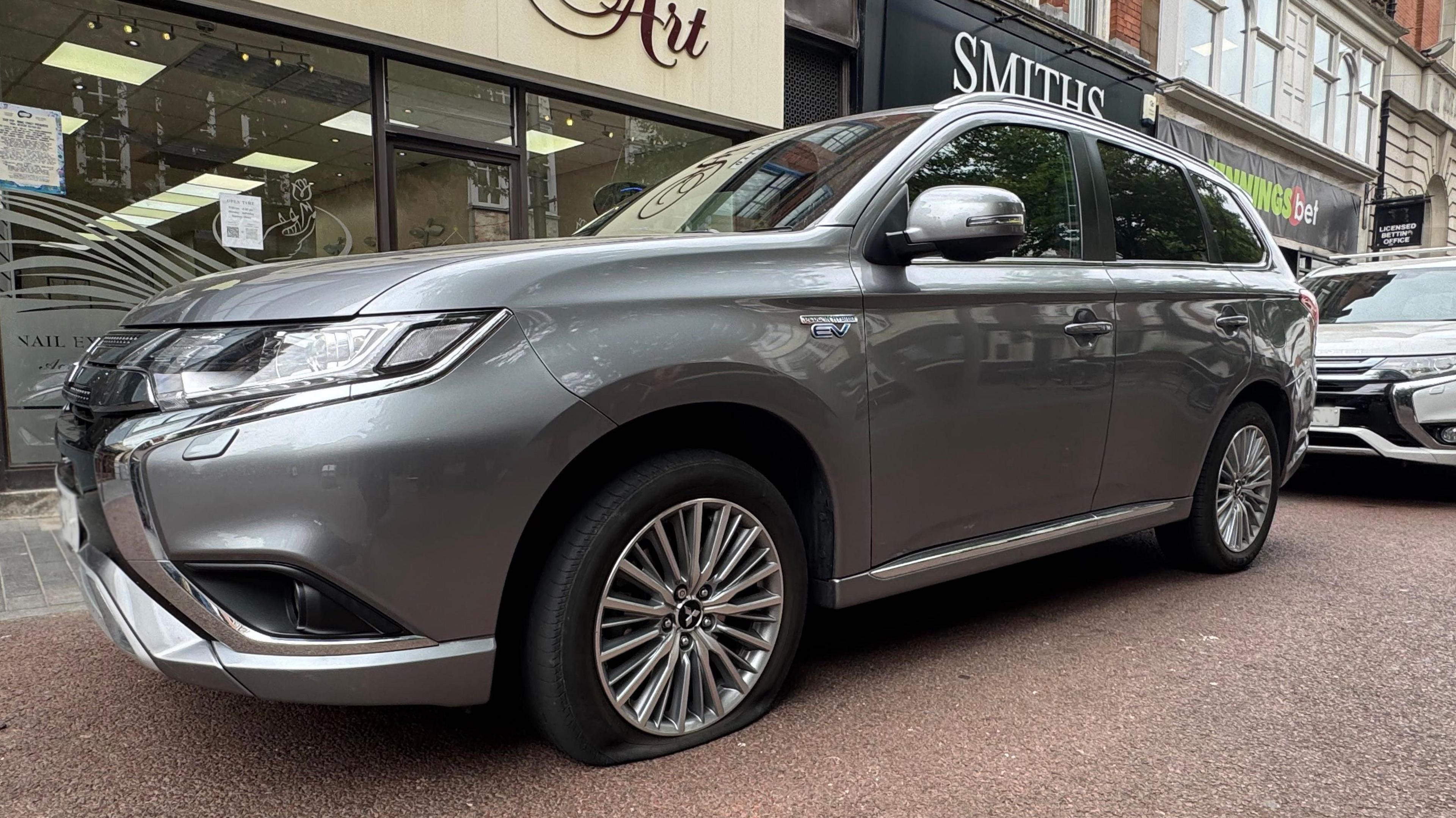 A silver Mitsubishi SUV with a flat tyre. 