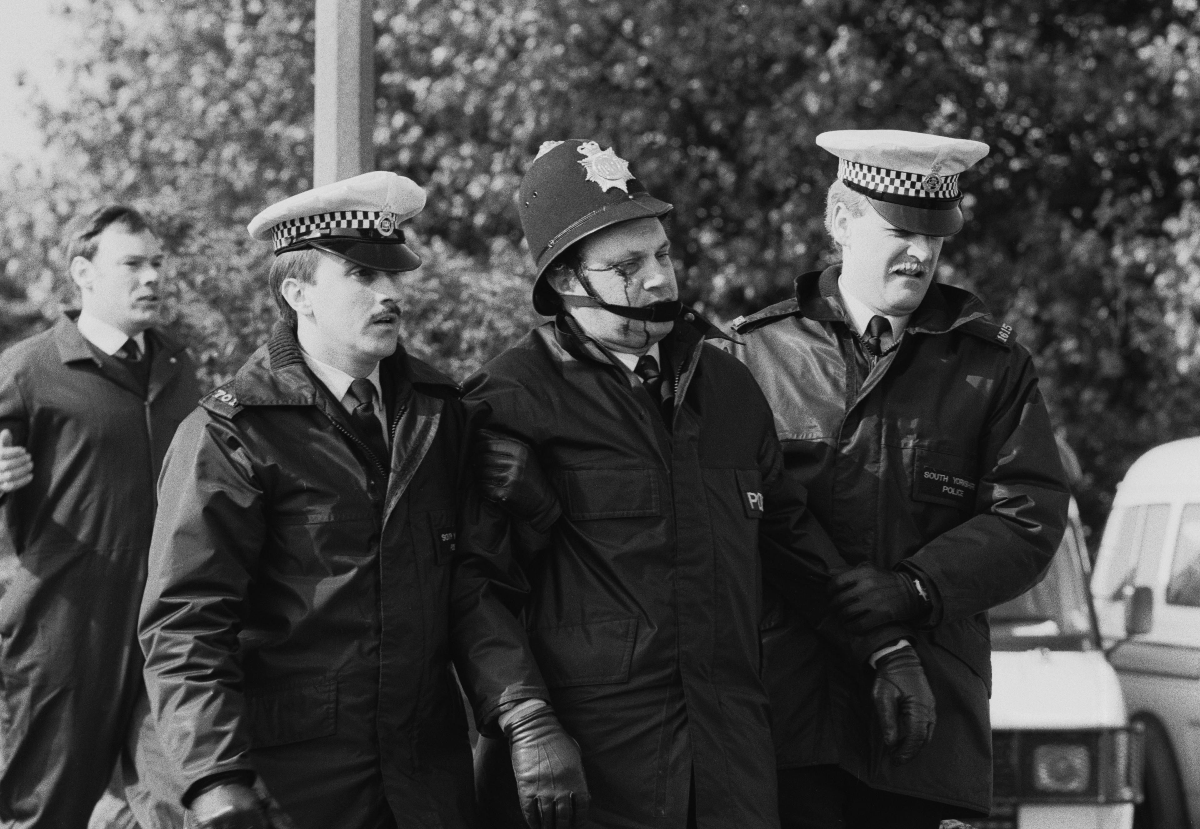 A police officer who has been injured is helped by his colleagues.