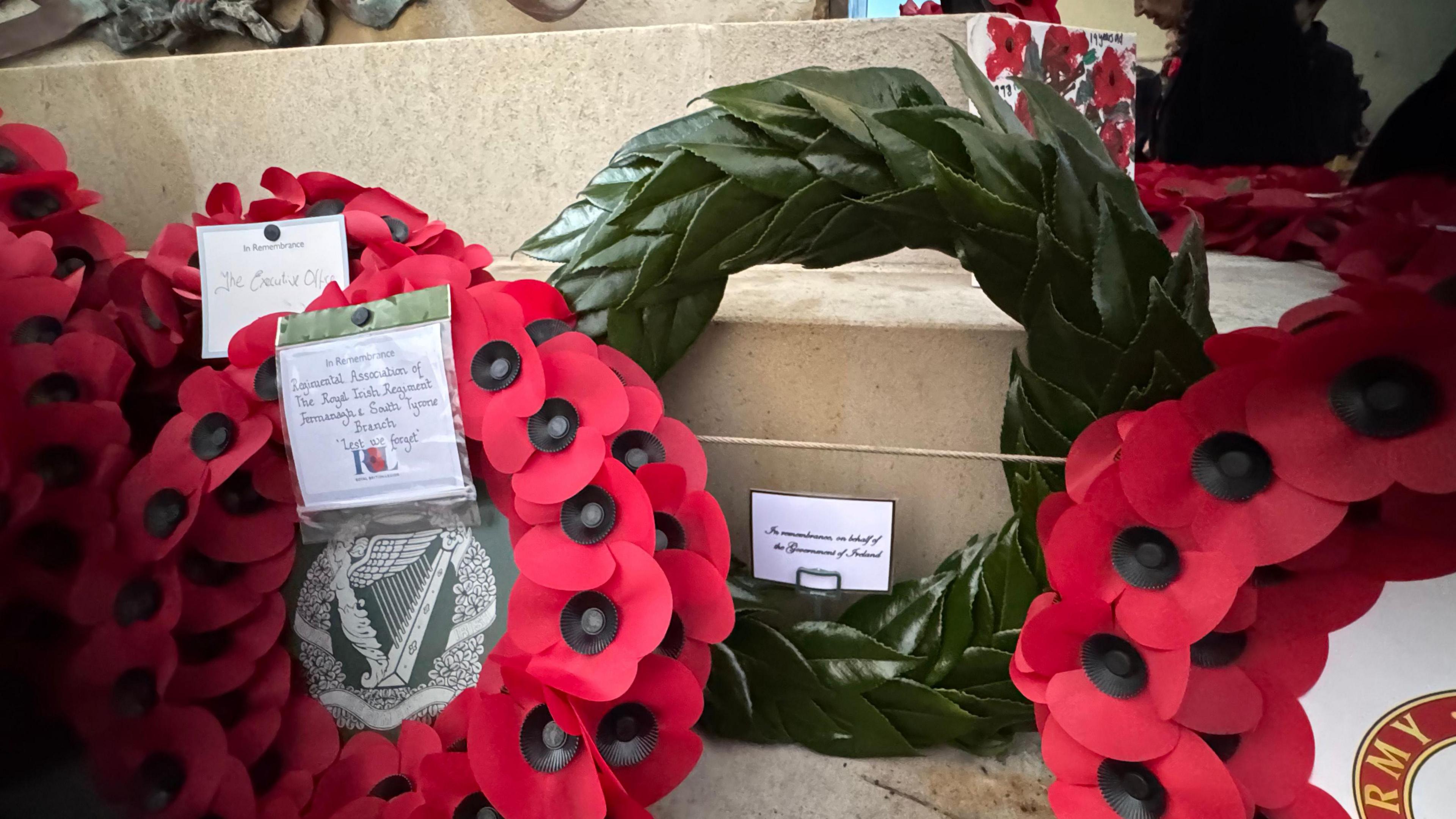 A green wreath among red poppy wreaths. On the wreath a note that reads "In remembrance on behalf of the government of Ireland"