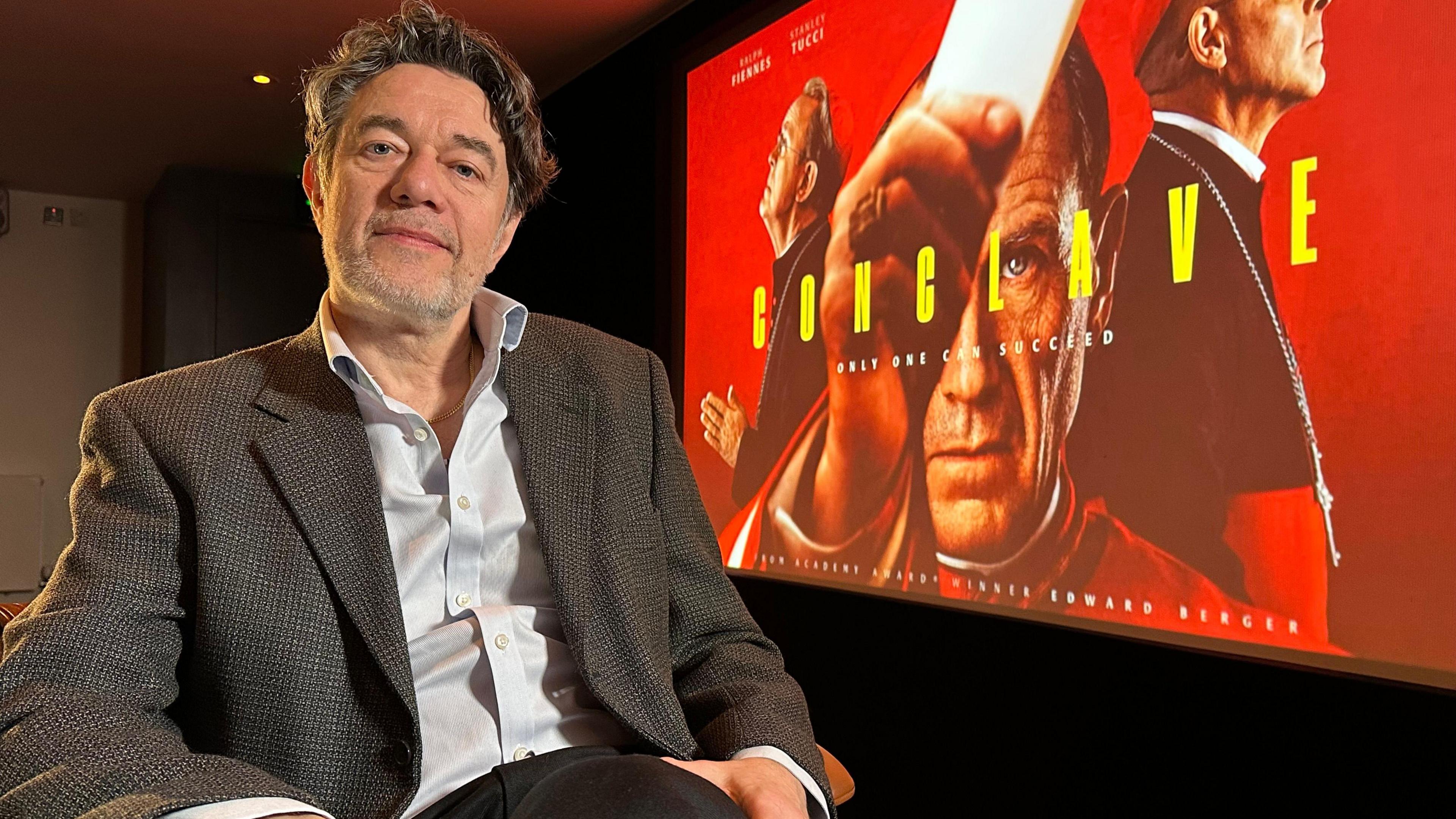 Peter Straughan sits in front of the poster for his latest film, Conclave. He's been visiting the Tyneside Cinema in Newcastle. 