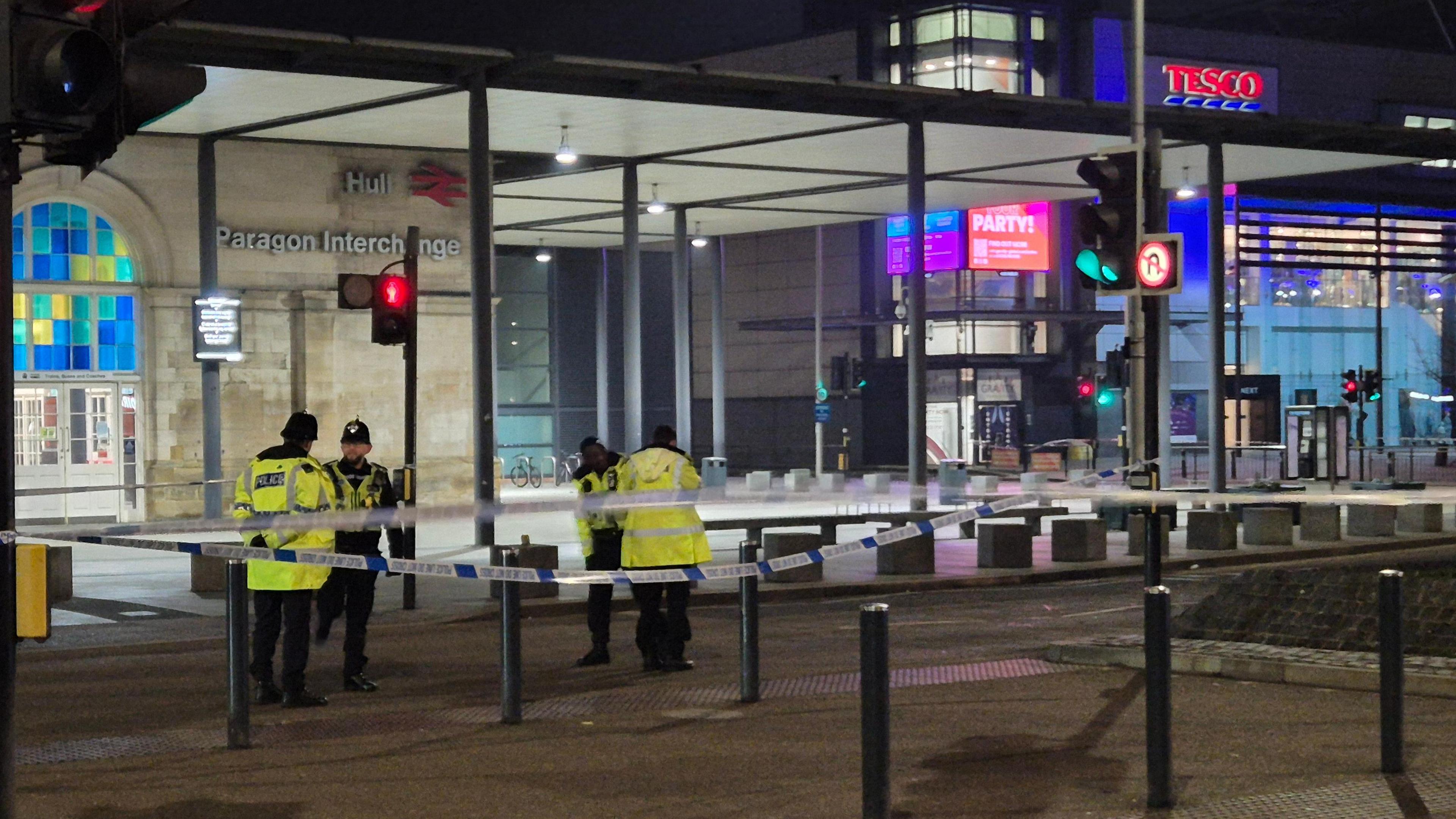 Four police officers standing behind a cordon, which is around Hull Paragon Interchange and St Stephen's Shopping Centre.