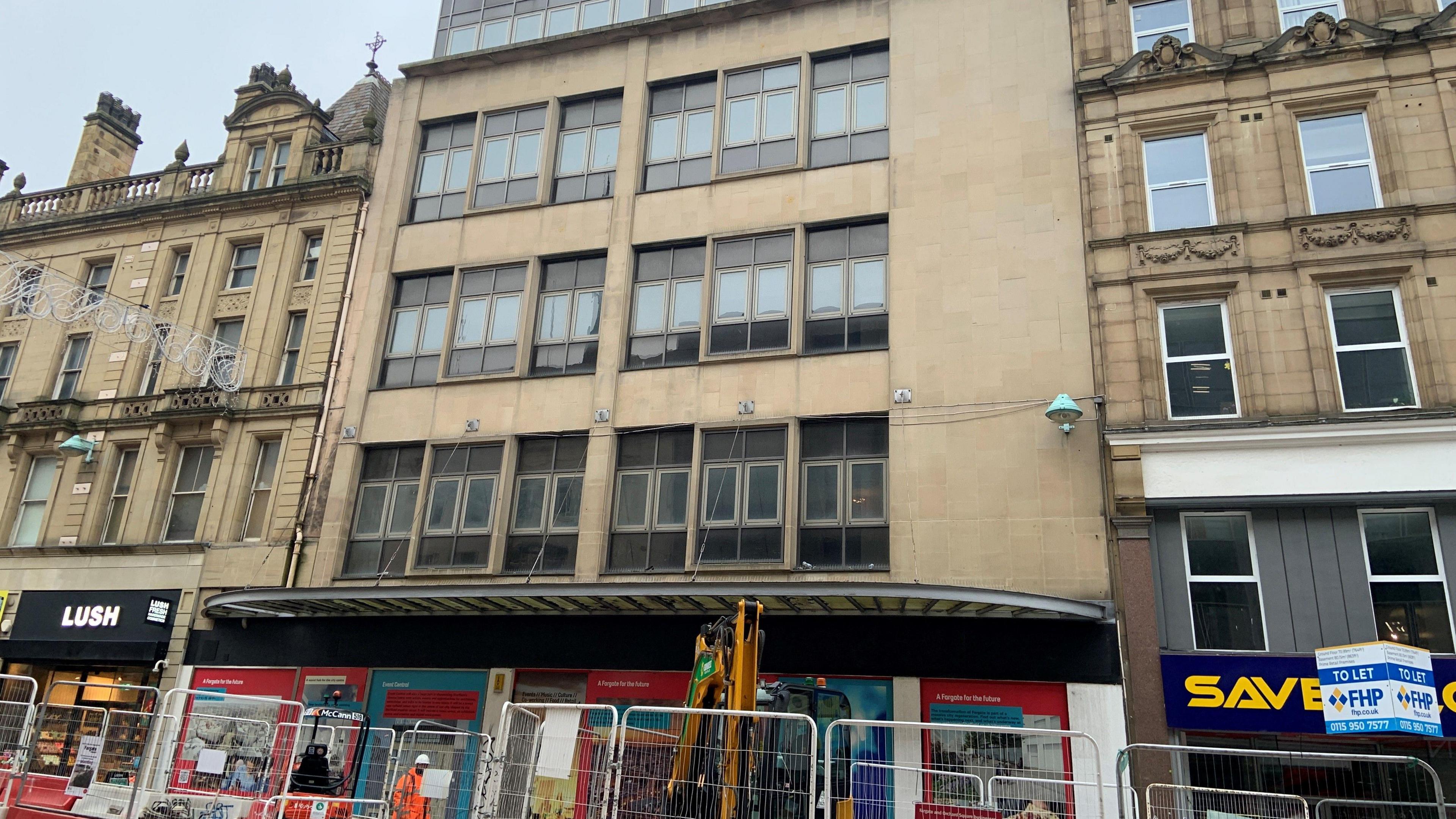 The outside of a building on Fargate, which is made from stone and has large windows. It looks old and in need of repair and there are fences and machinery outside