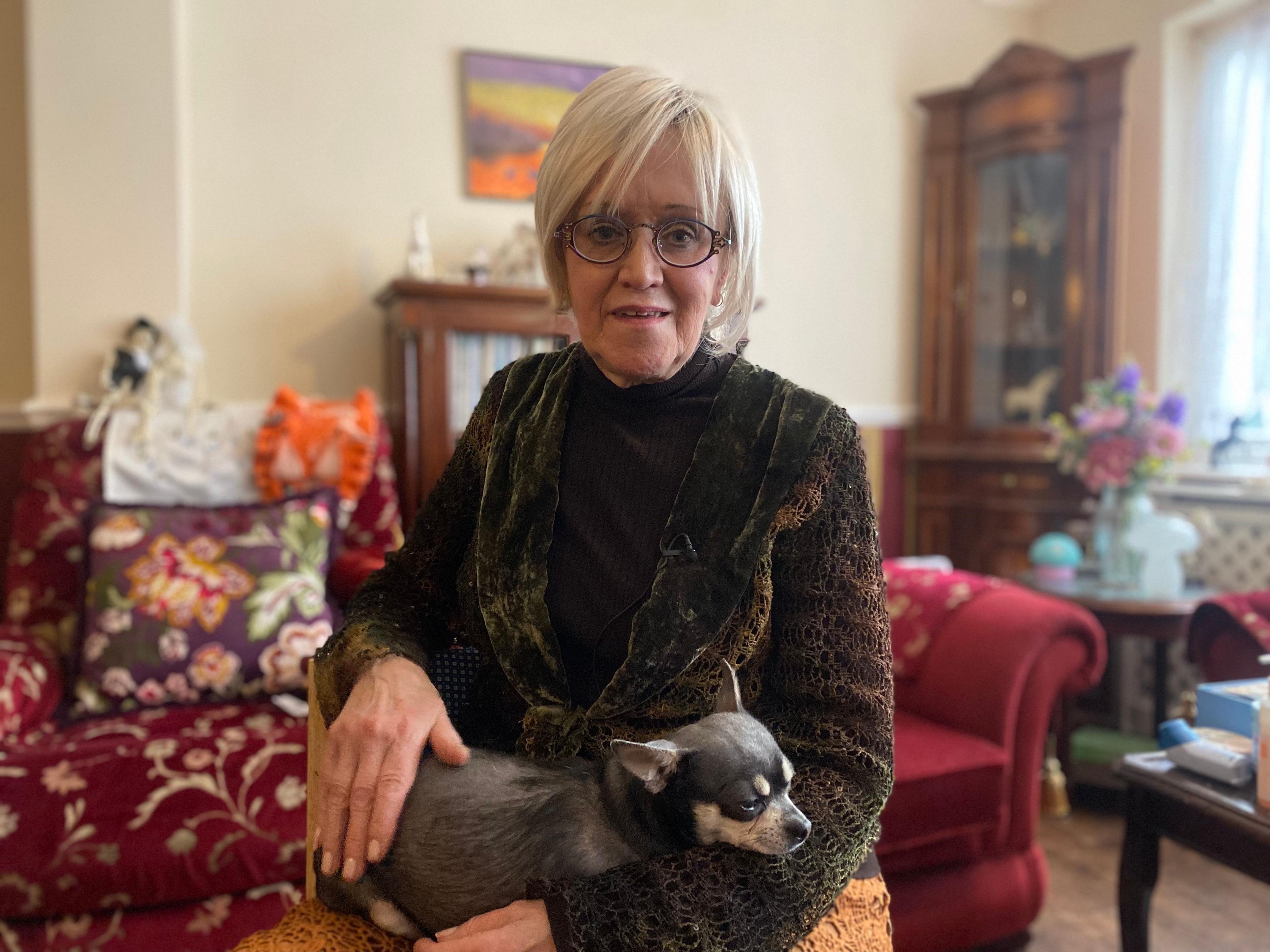 Babs Thwaites, on sofa in her home with her dog.