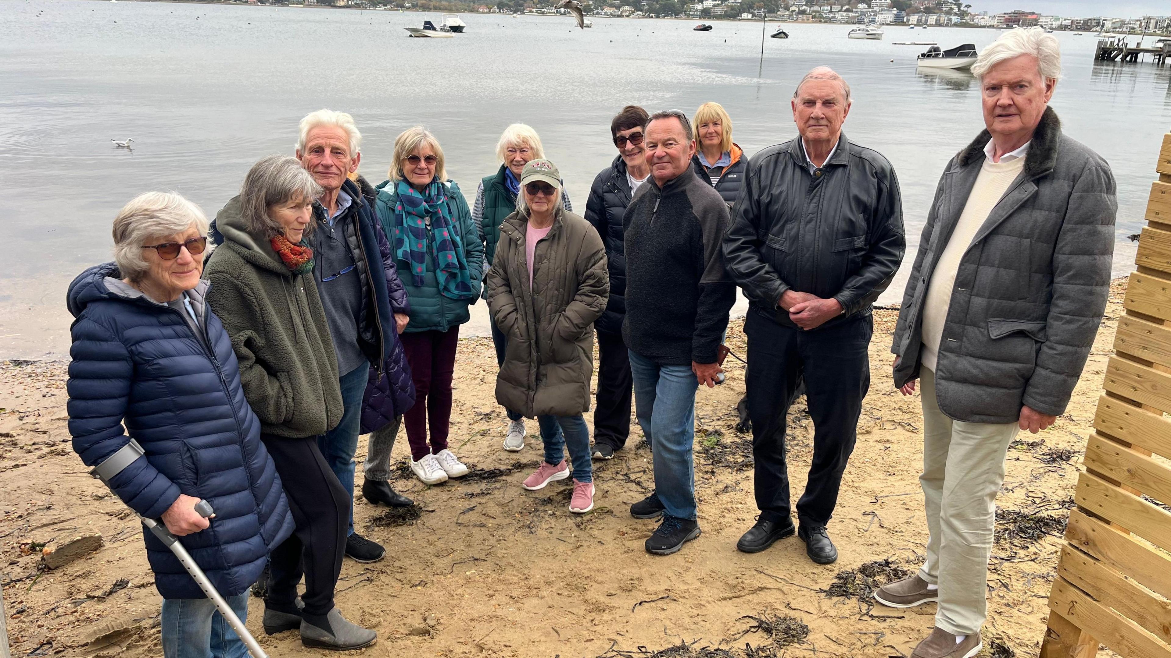 The group of residents who are against the fence stood next to it and on the beach near the water.