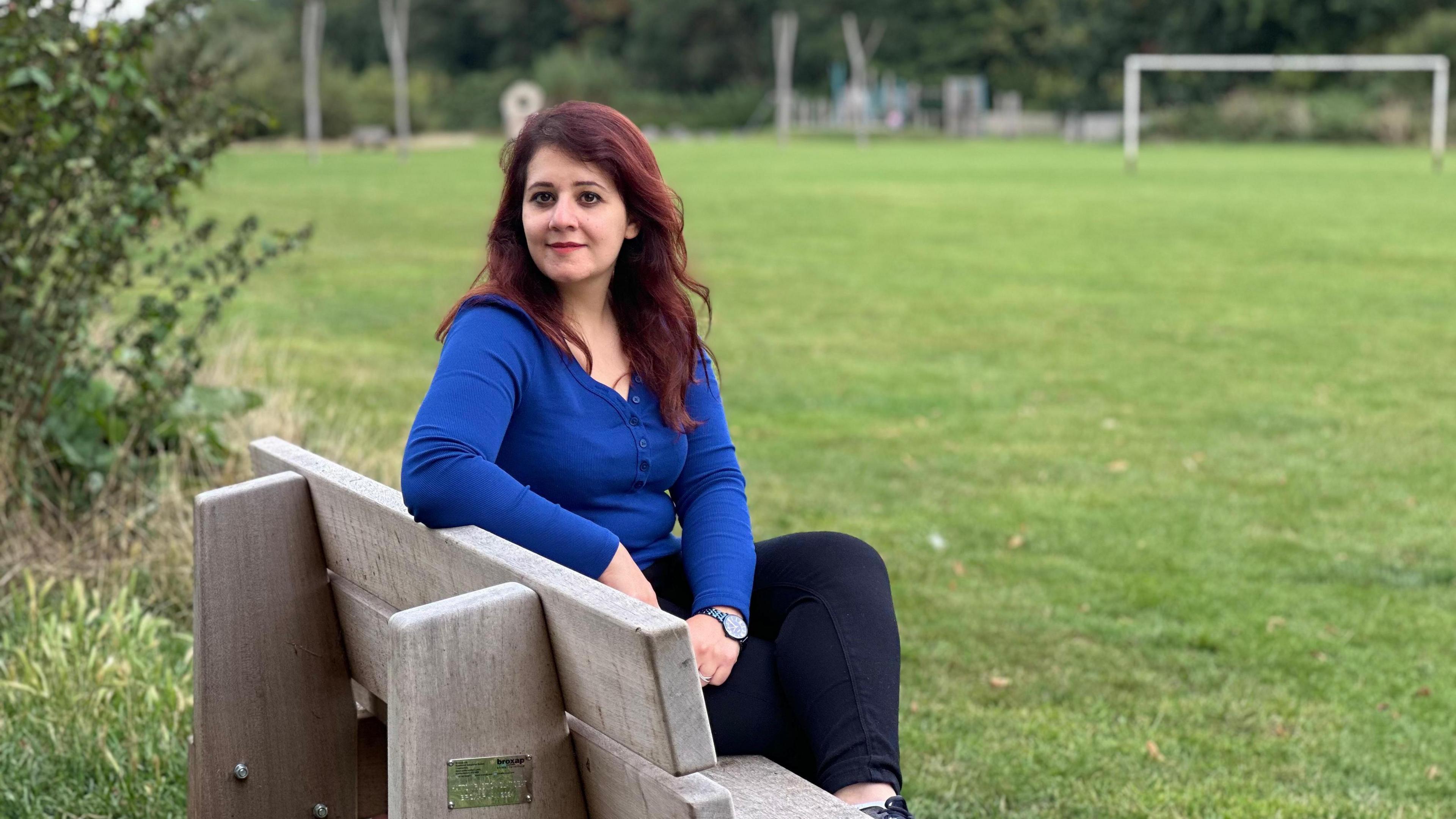 Zina Abdulla sitting on a bench in a park wearing a blue top and black jeans