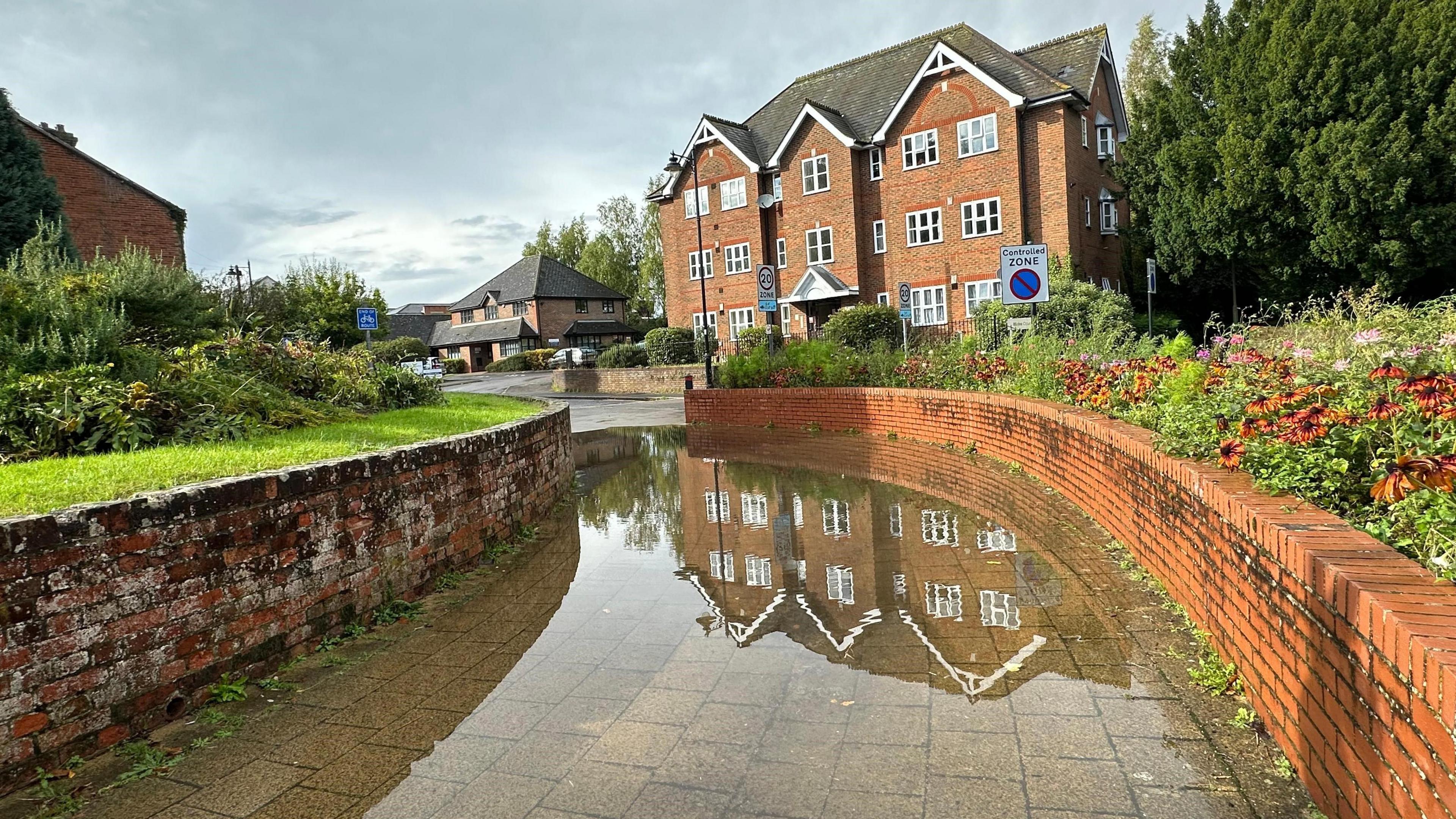 A path with a brick wall either side, which has been submerged under a few centimetres of water.