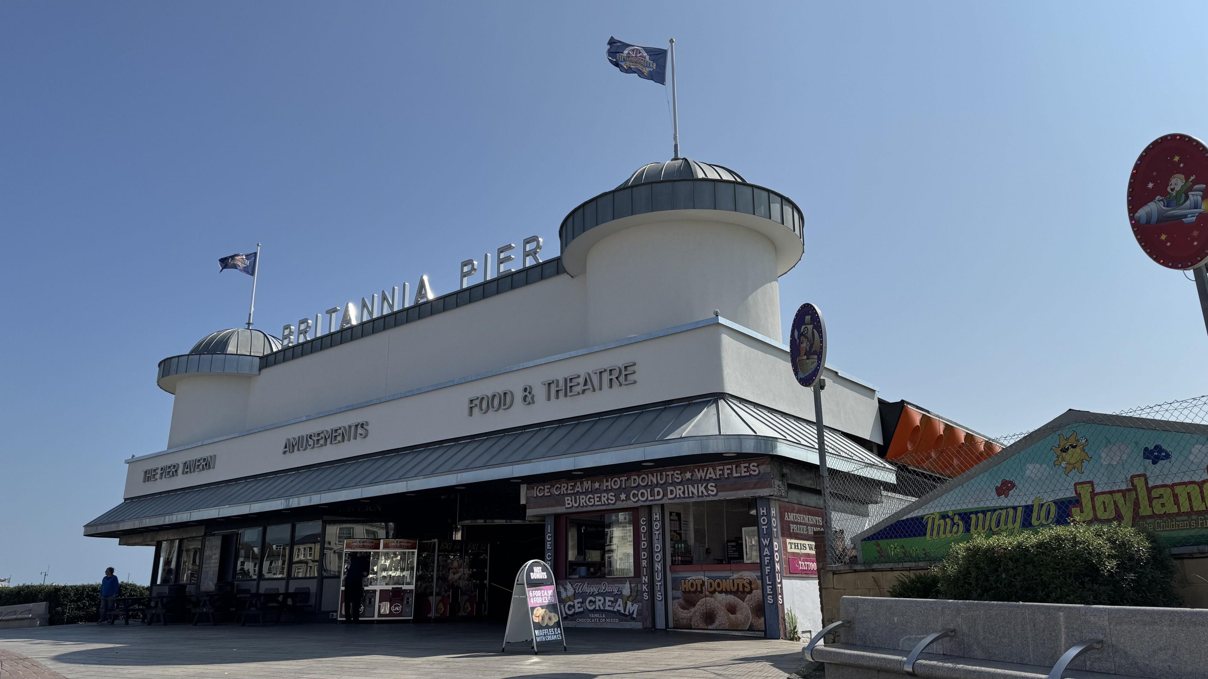 View of the new facade of Britannia Pier from the front on the right. The entrance is now white and has a sign that says Britannia Pier above the entrance.