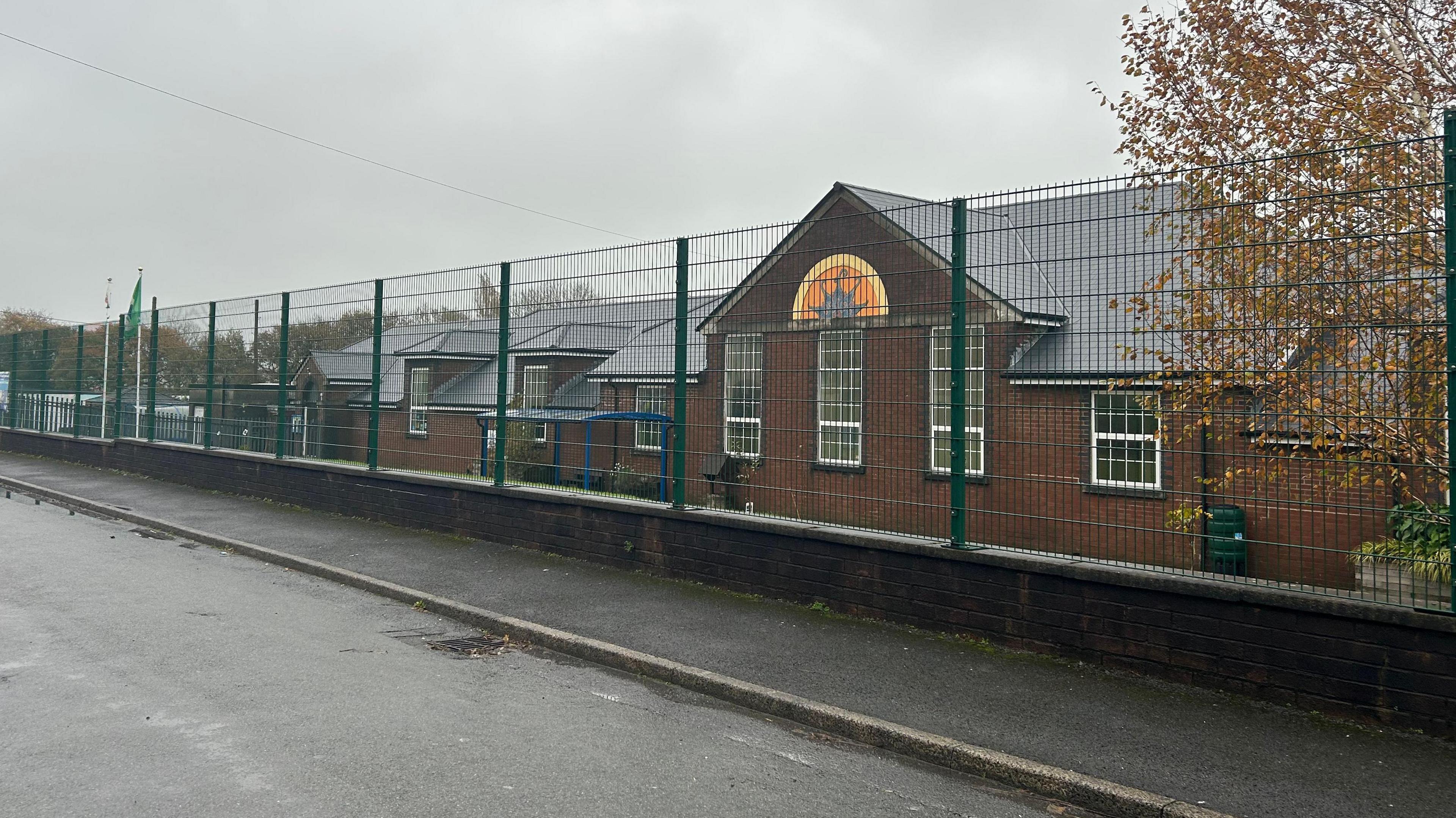 Dafen Primary School, a red brick single-storey building, sits behind a green fence.