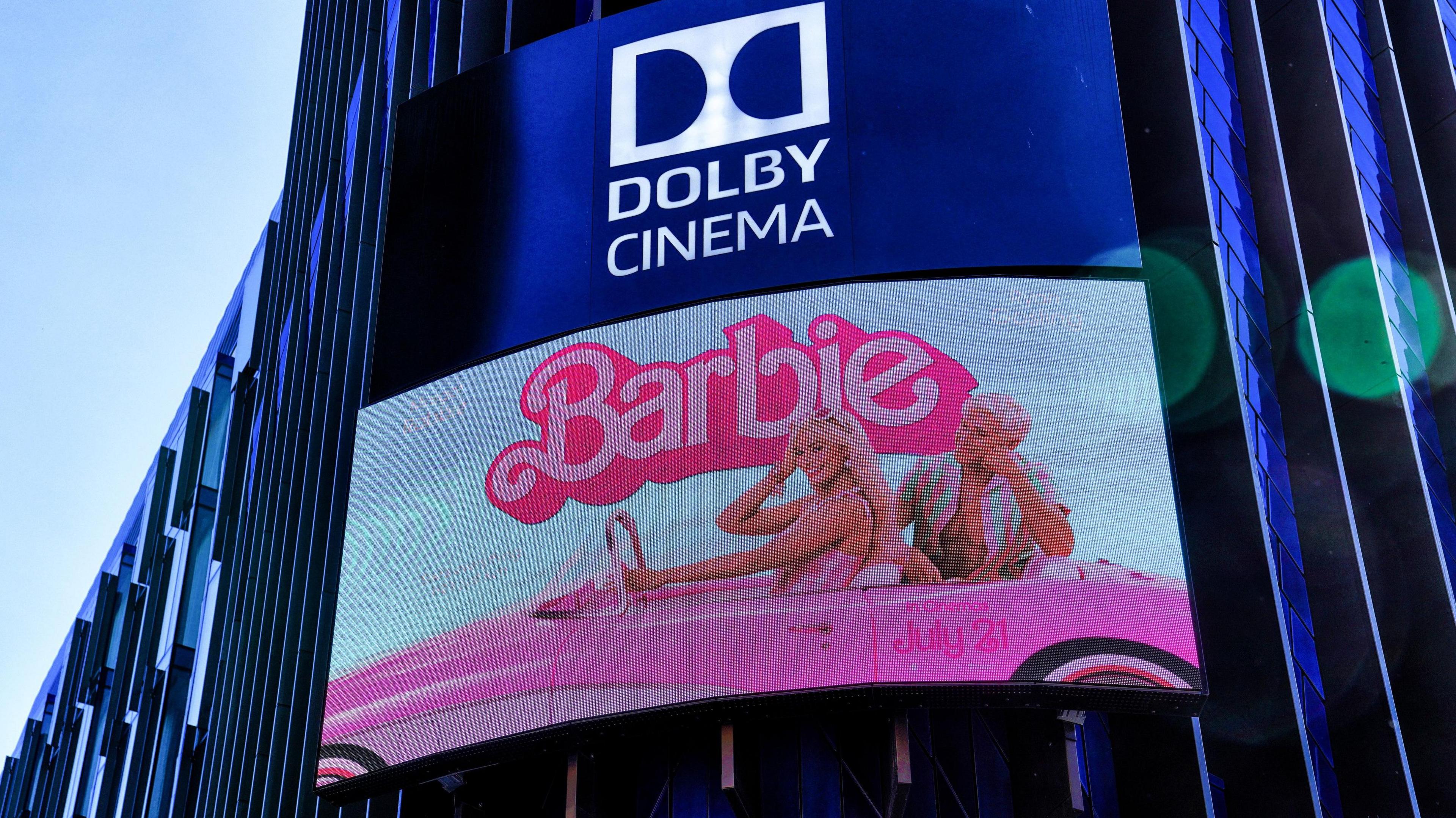 A TV screen poster of the film Barbie on the outside of the Odeon Cinema building in Leicester Square. It features Margot Robbie, driving a pink car and Ryan Gosling in the back seat.