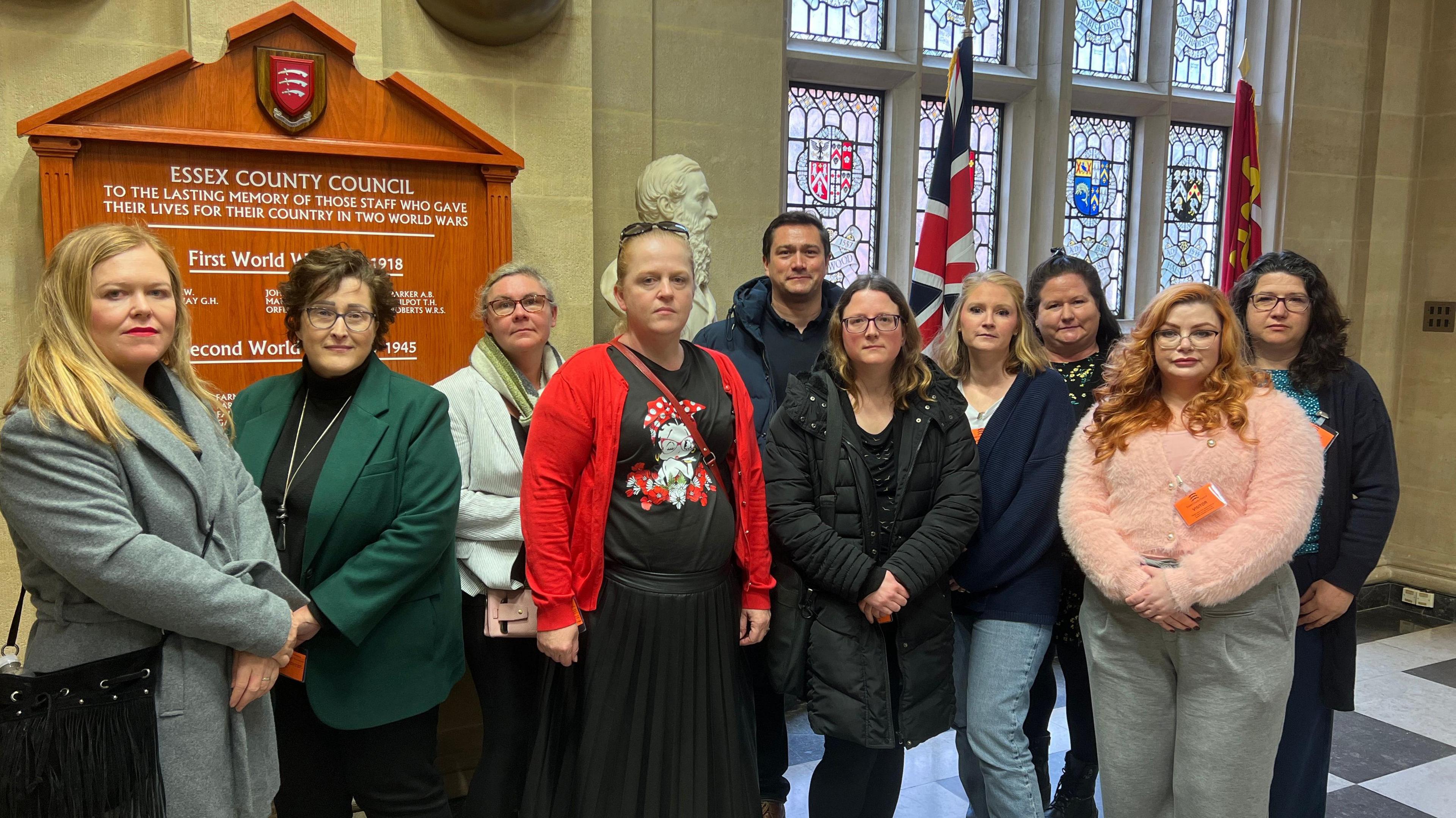 A group of about a dozen parents, mostly mums, posing for a photo in the corridor of County Hall. There are flags and a stained glass window behind them.
