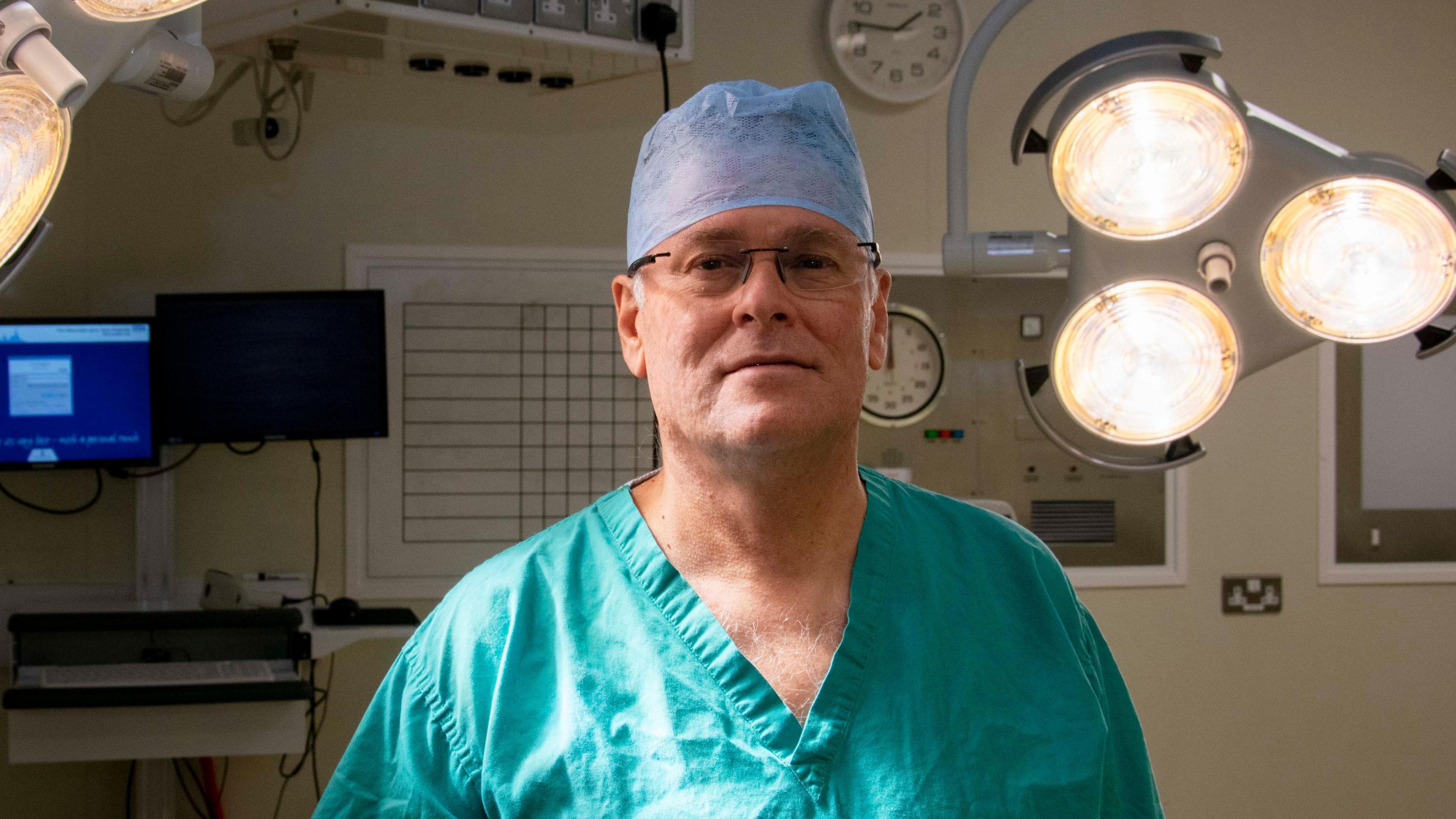 Professor Francisco Figueiredo, a Consultant Ophthalmologist at Newcastle's Royal Victoria Infirmary. He is wearing his green surgical scrubs and his surgical hat and is in an operating theatre. He is looking at the camera with the theatre lights on above him,