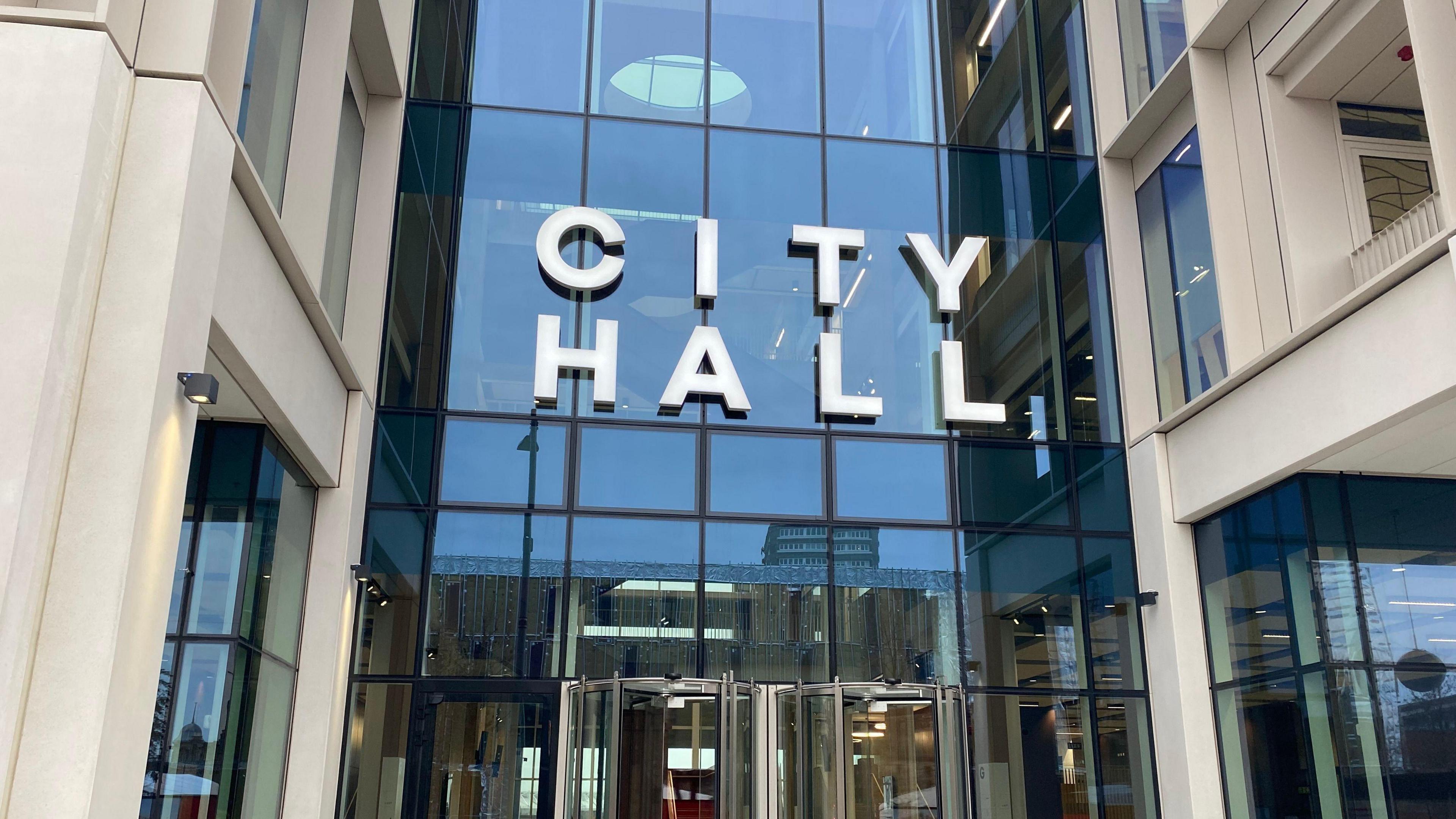 The entrance to Sunderland City Hall. The entrance is glass fronted and has revolving doors. A sign reading CITY HALL hangs above the entrance in large white letters.