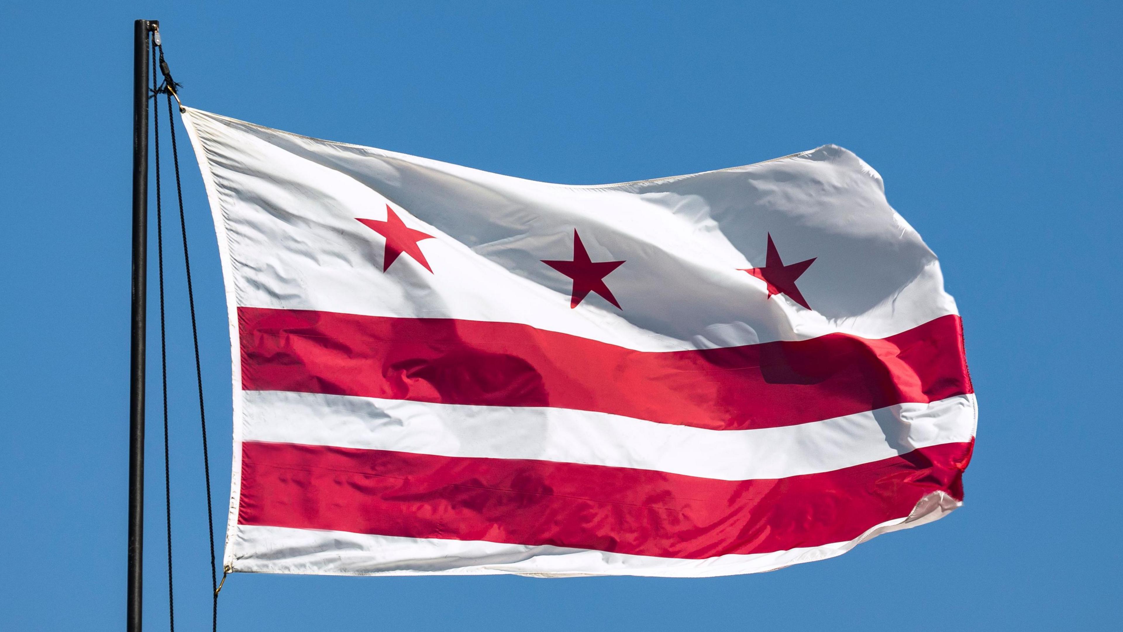 A white flag with three red stars above two horizontal red stripes flutters in the wind.