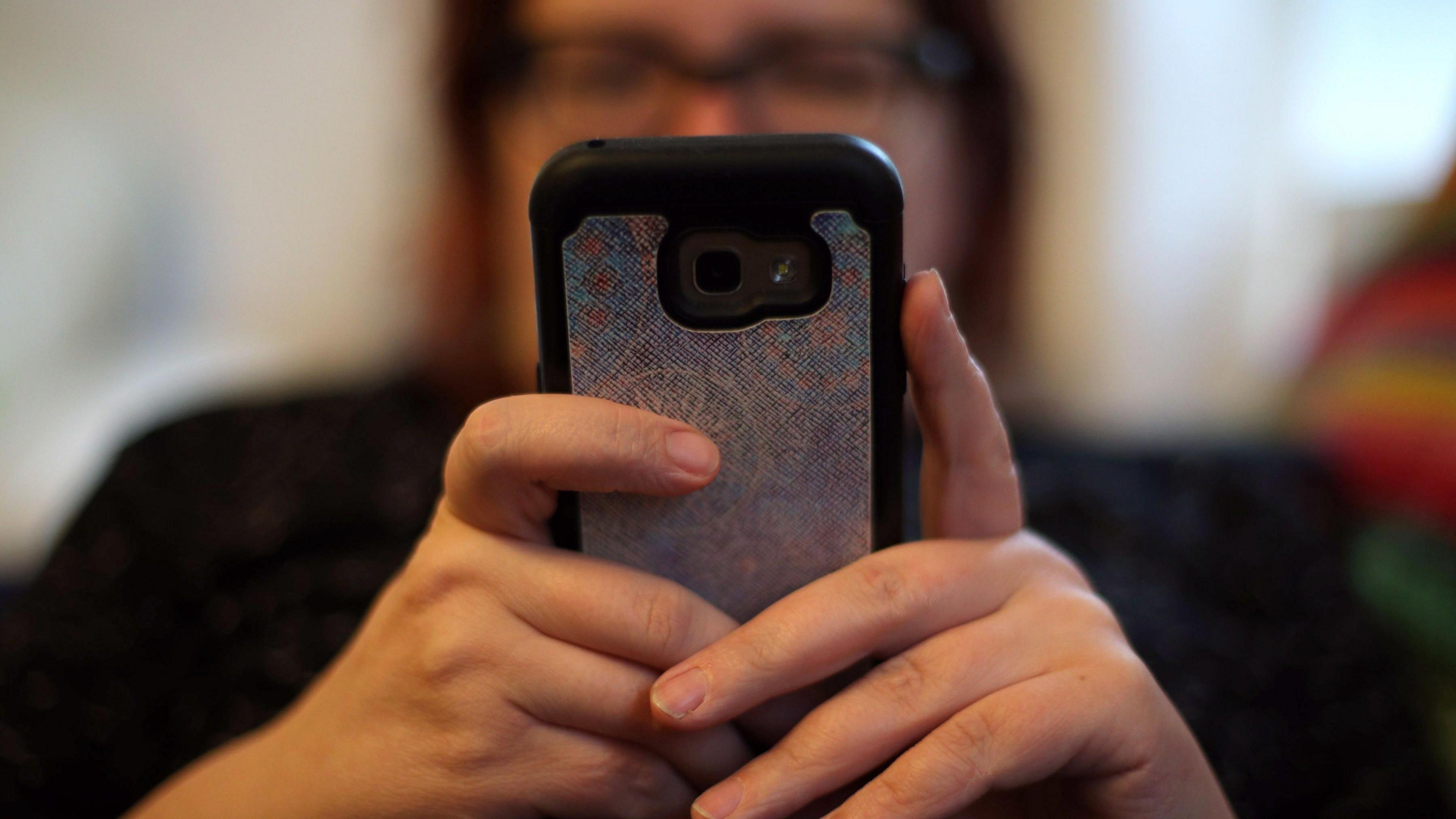 A woman holding her mobile phone between her hands, which are in focus, and her face and body are not.