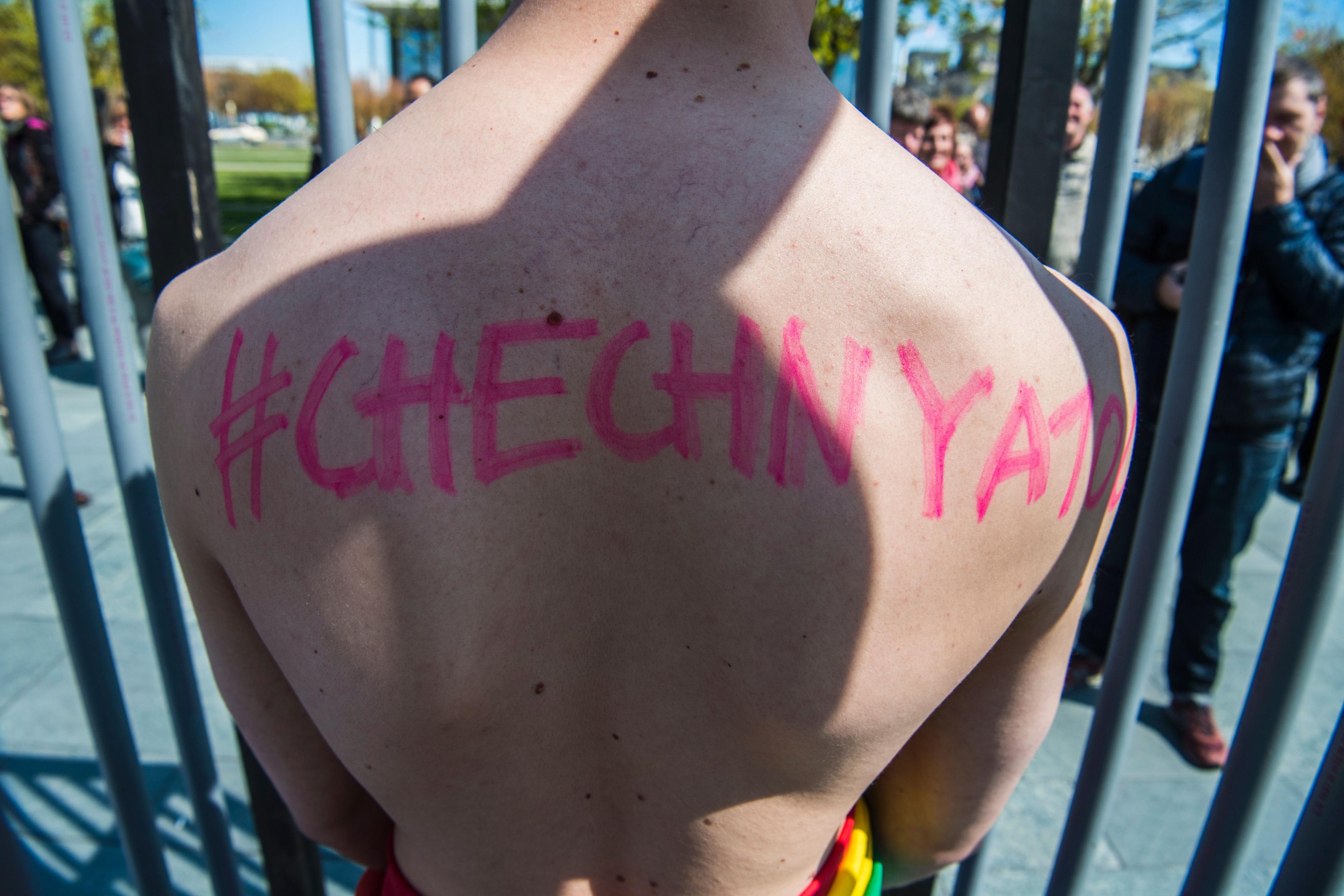 An activist stands naked, wrapped in a rainbow flag, in a mock cage in front of the Chancellery in Berlin