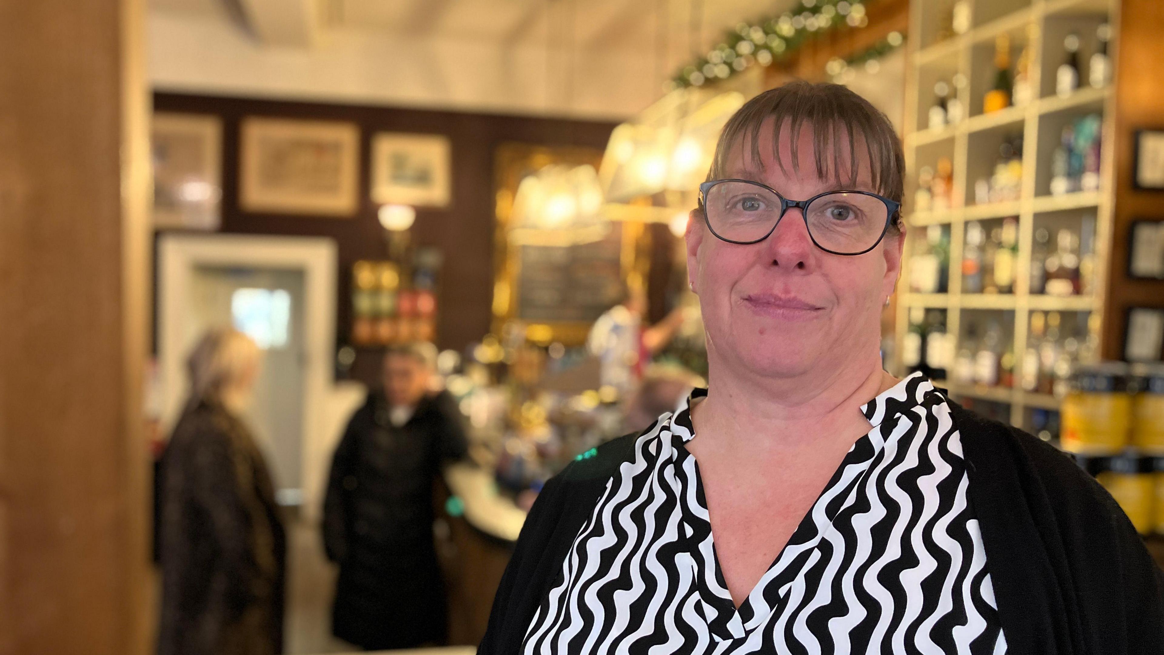 Melissa Dixon, general manager of The Royal Hotel, pictured inside the the hotel. She is wearing a white top patterned with black wavy vertical lines. She has glasses and short hair with a fringe.