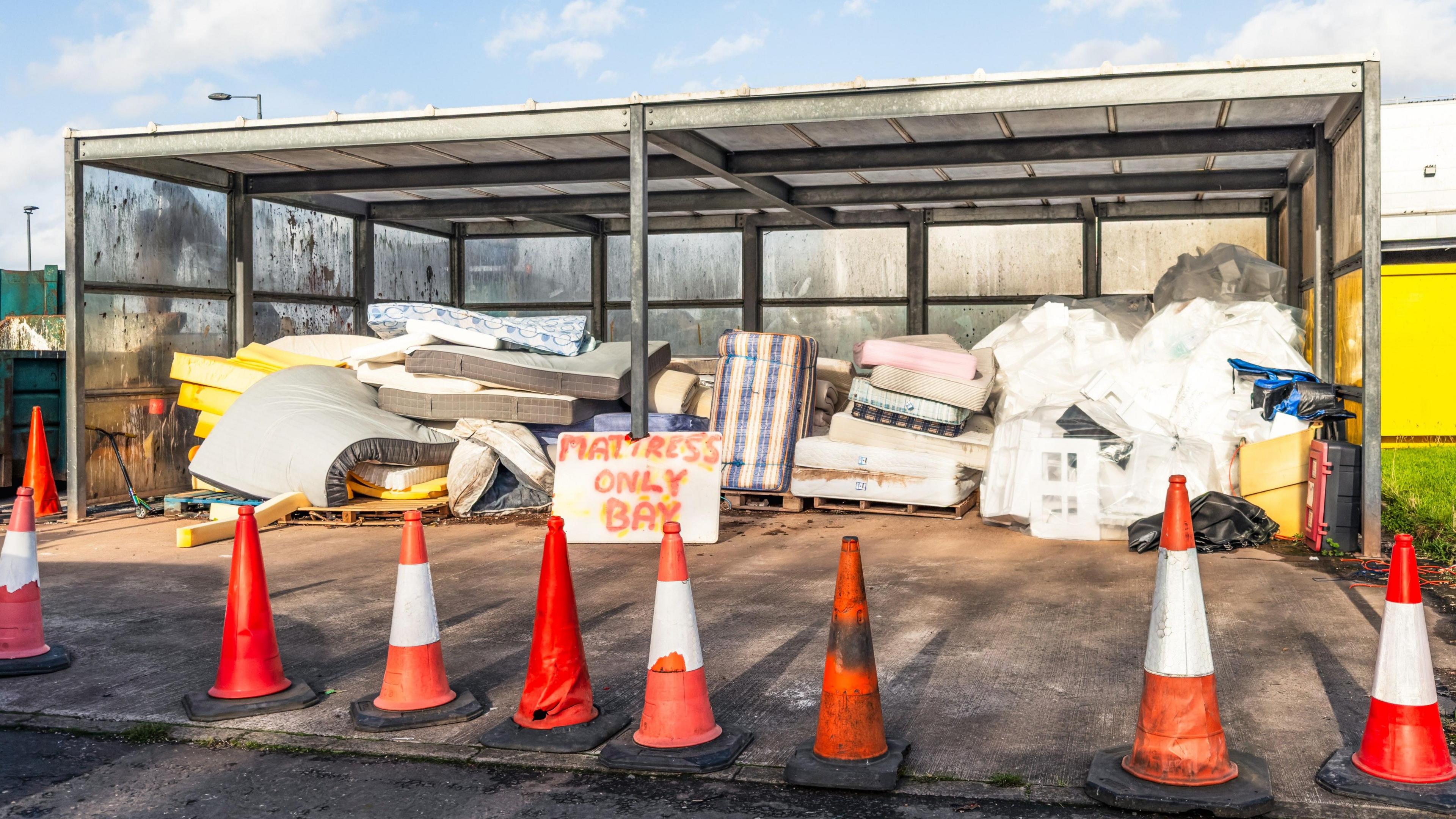 A large collection of used mattresses in a sheltered area of a waste recycling centre.