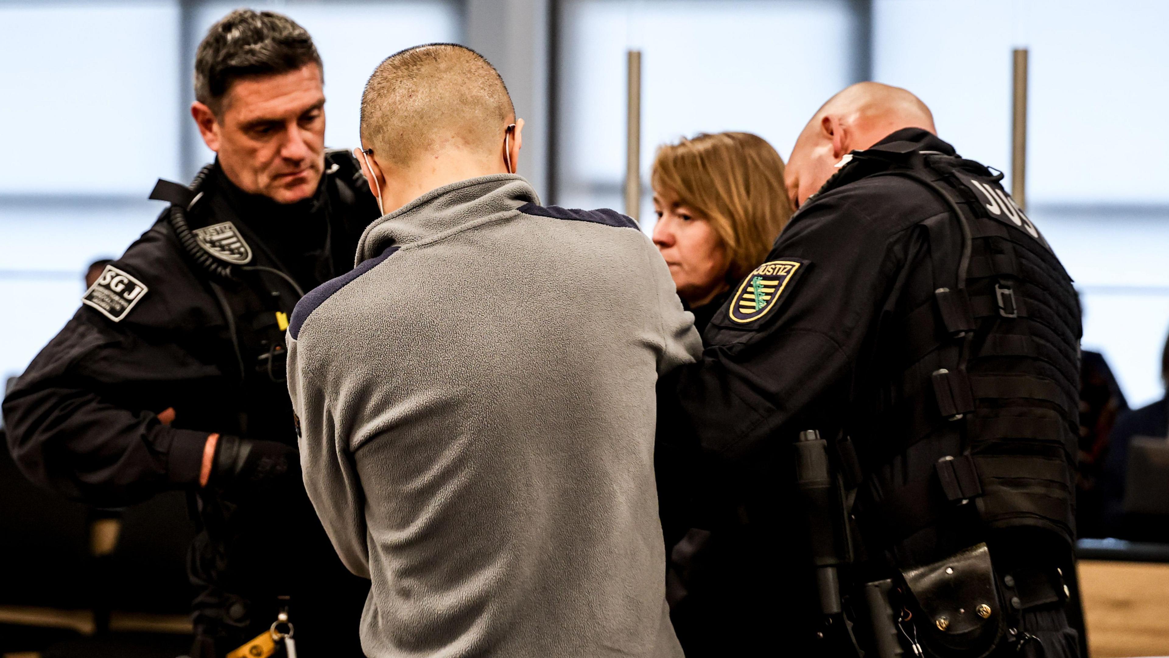 A man is seen from behind standing in front of three prison officers.