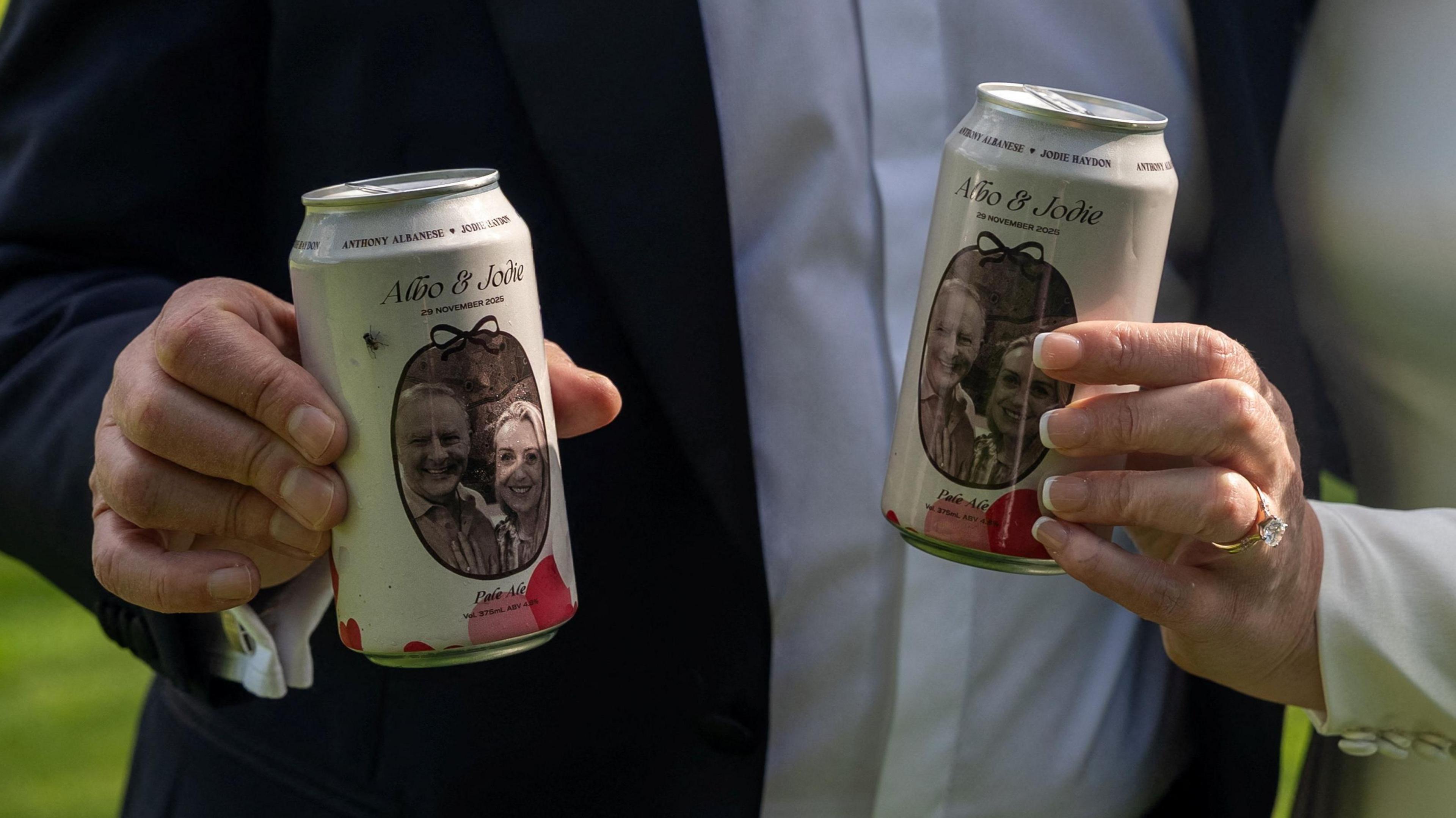 A close-up image of two custom made beer cans featuring images of Albanese and Jodie Haydon