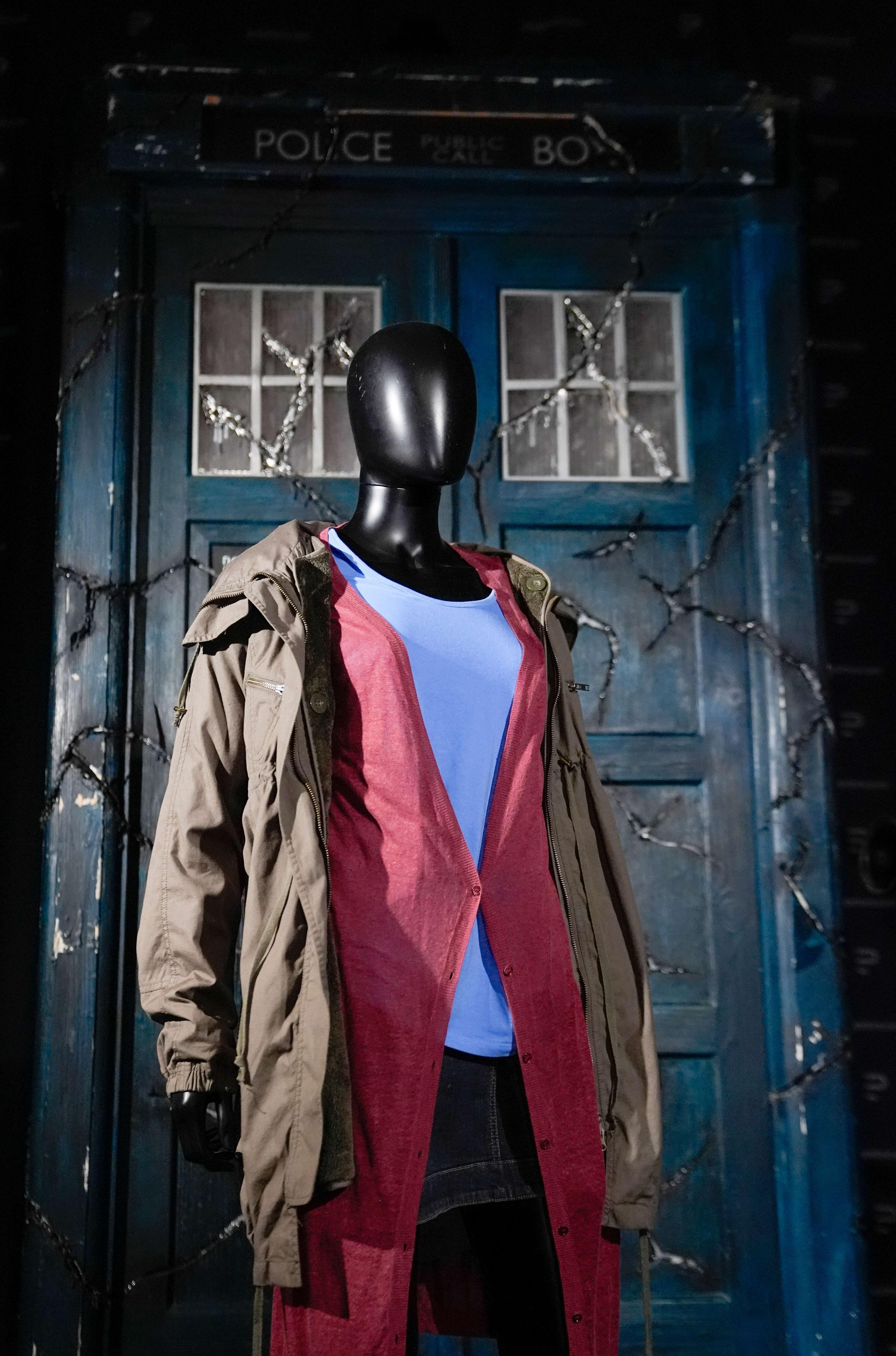 An Amy Pond costume from Doctor Who series five, episode seven: Amy's Choice. Displayed on a mannequin, the costume comprises a denim skirt, a white t-shirt, a long red cardigan, and a brown parka