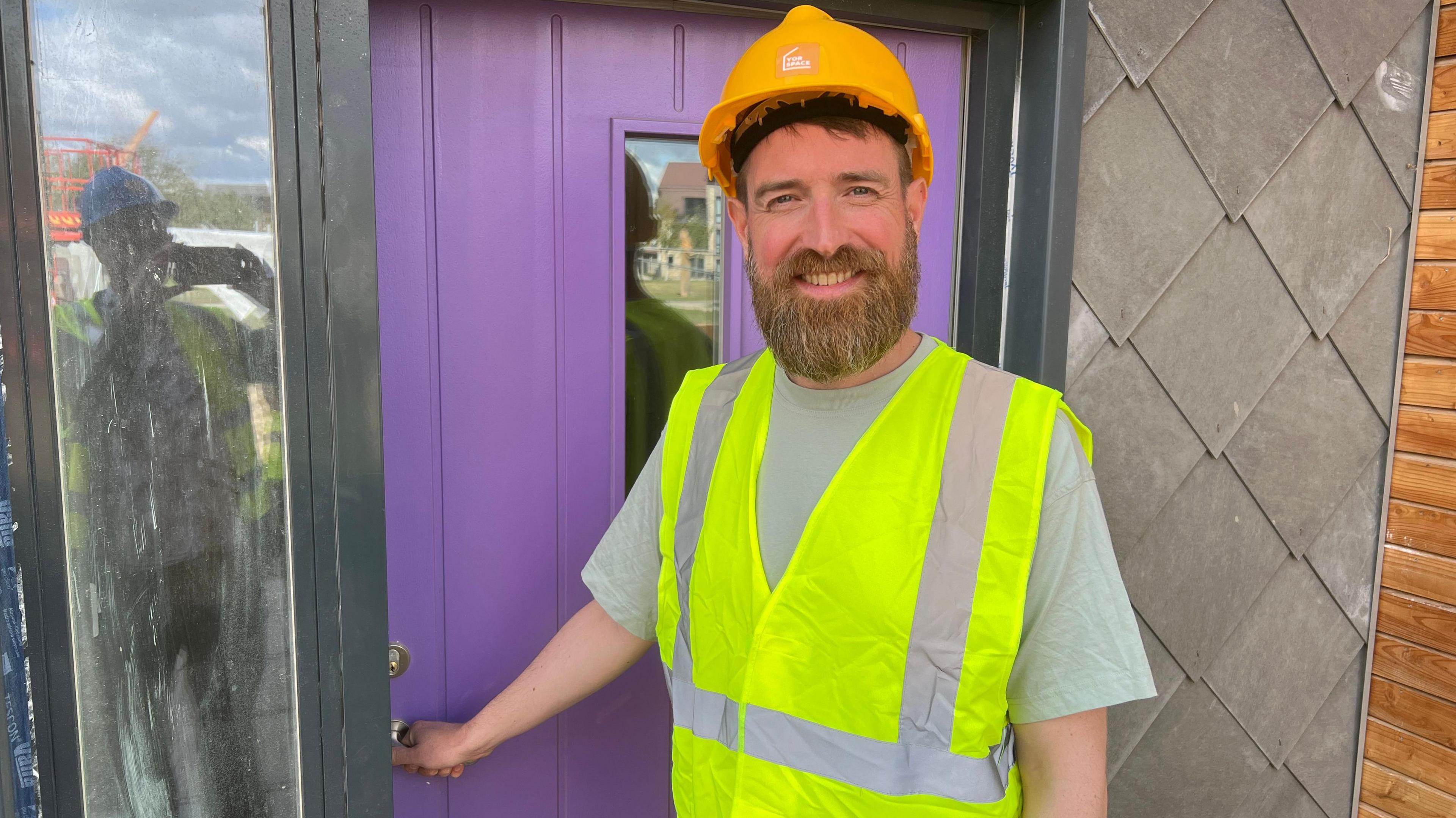 Yorspace co-founder James Neward is standing outside his home at Lowfield Green, York. The front door is painted lilac. He is wearing a hard hat and a high-vis vest.