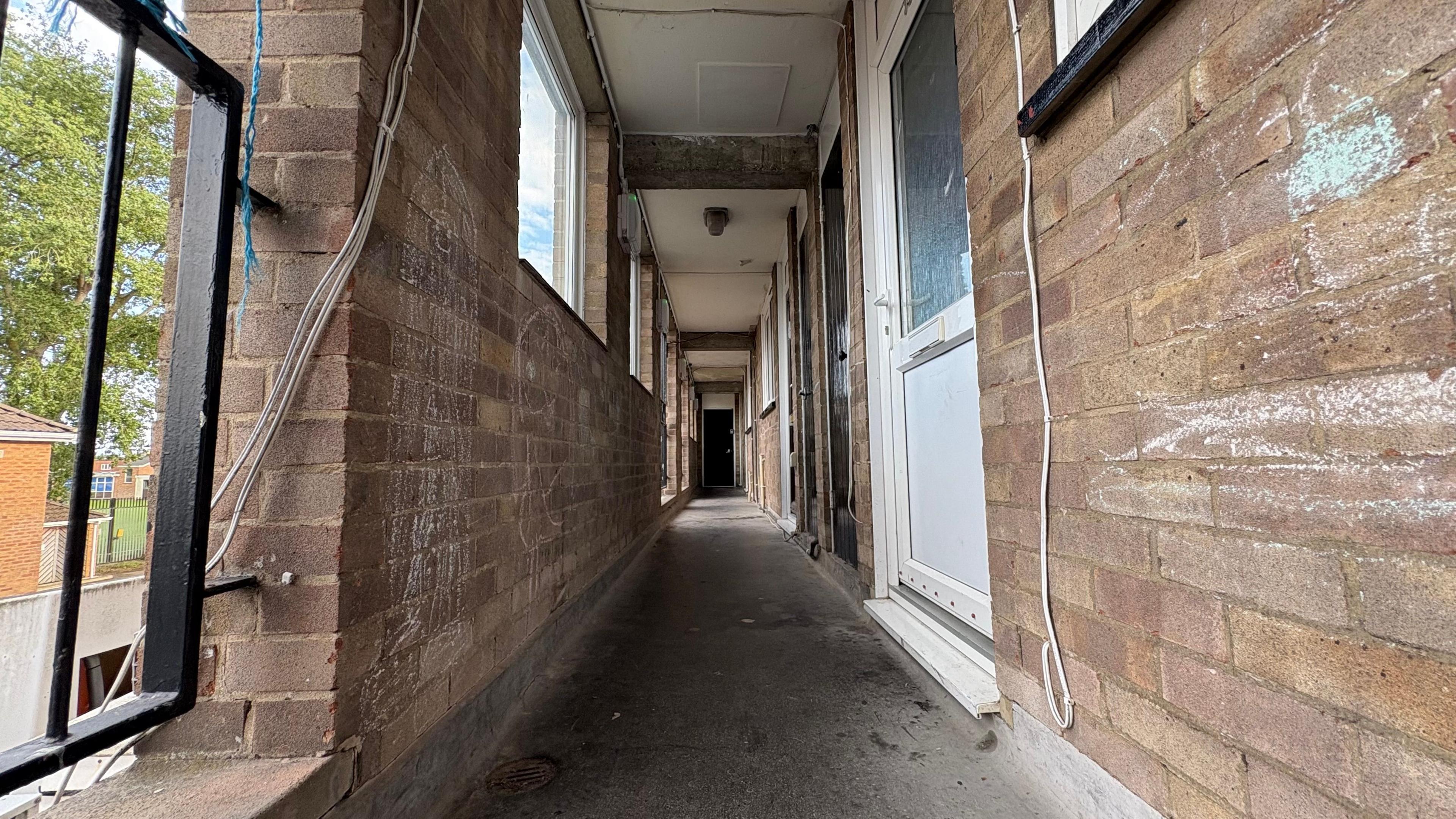 A view of a corridor in the block of council homes. Children have drawn on the brick walls in chalk.