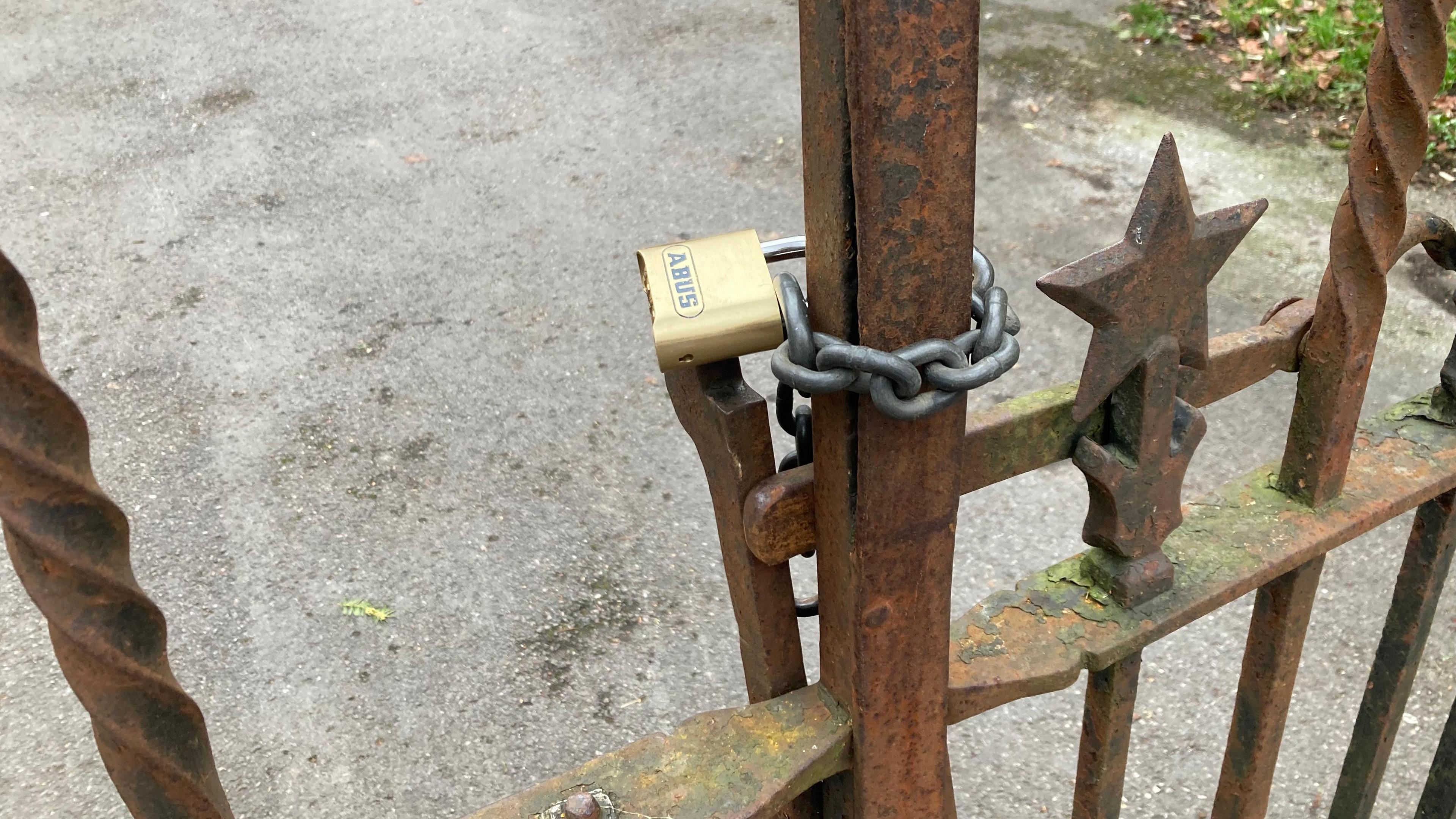 A gold padlock with a chain around it holds a rusty victorian gate closed