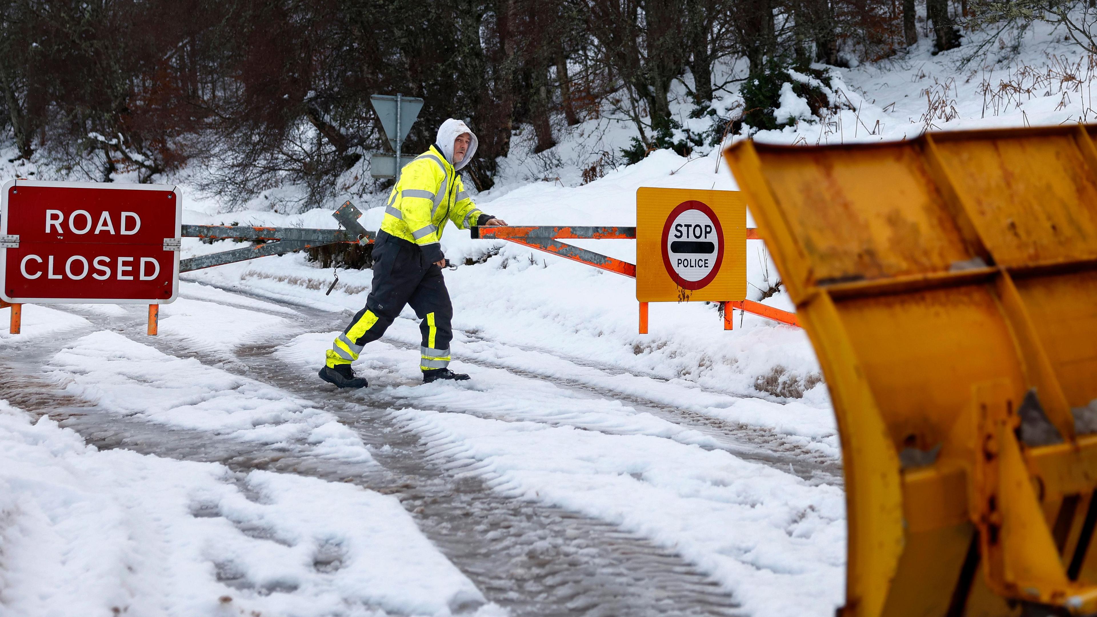 A man closing snow gates on a snow covered road with a snow plough.