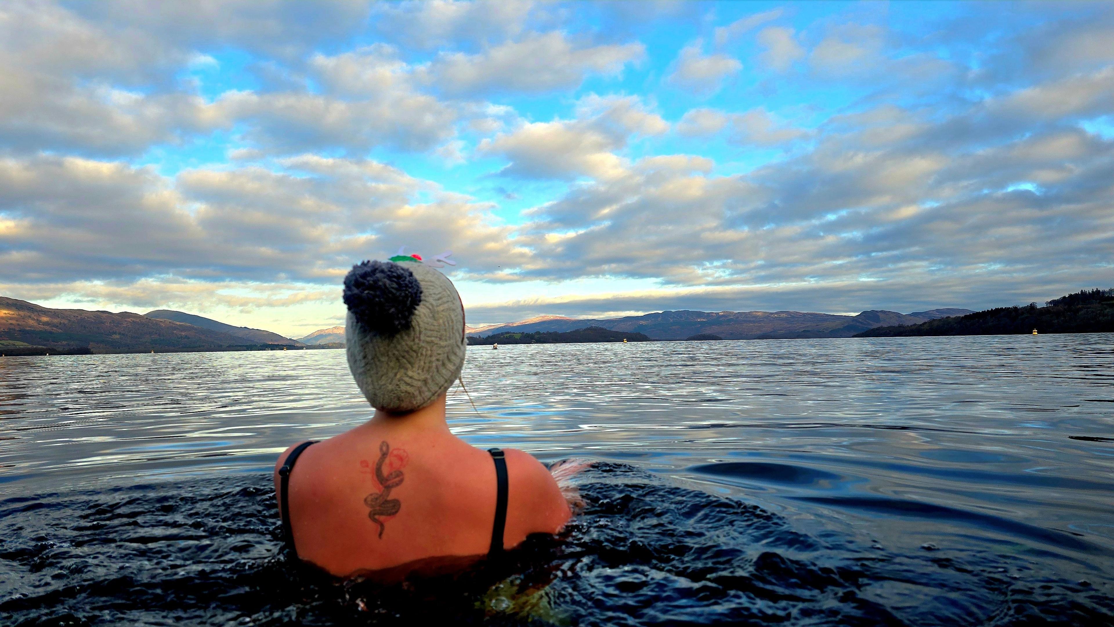 A view of the back of a swimmer in a lock on a clear and sunny day. The swimmer has a tattoo on her back and is wearing a hat.