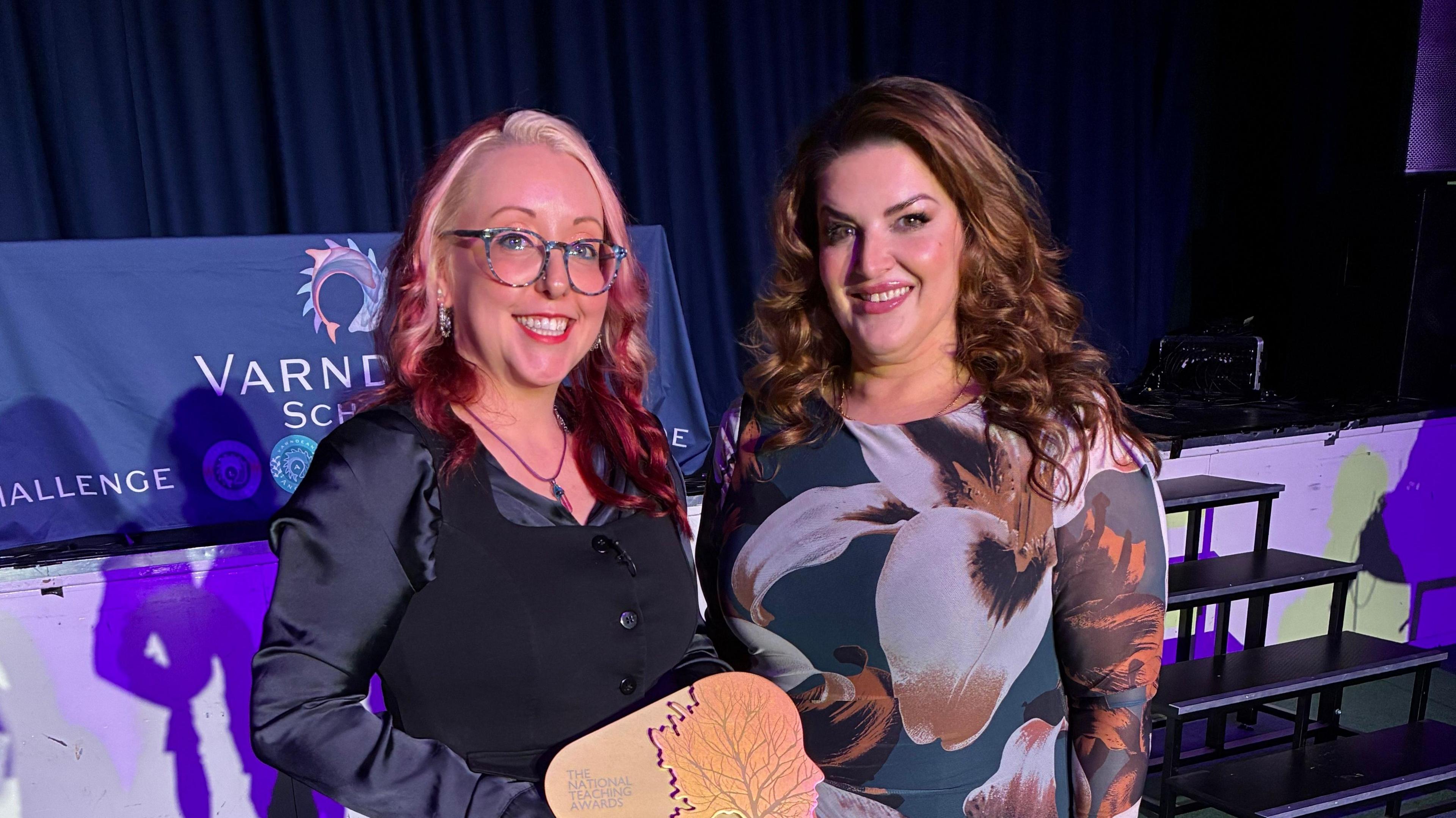 Jolie Bartley, Head of Performing Arts at Varndean School, pictured with West End star Jodie Prenger. The pair are pictured at Varndean School and Jolie is holding her award. Jolie is wearing a black top and has blonde/red dyed hair. Jodie is wearing a flowered dress and has long brown hair.