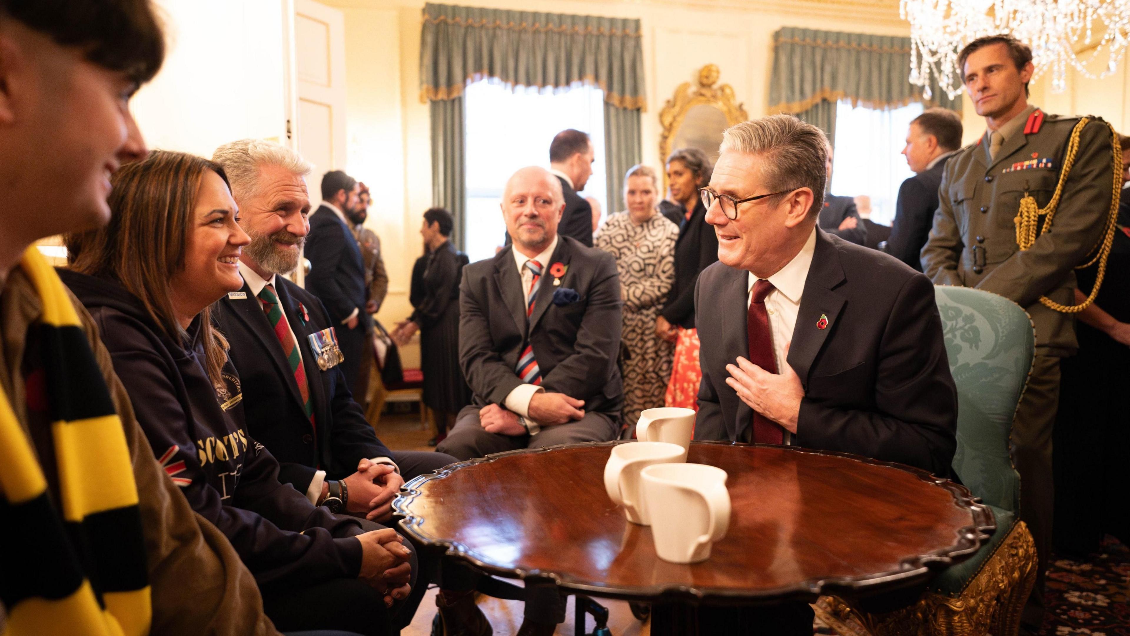 Sir Keir Starmer chats to veterans and charity representatives in Downing Street. Four people are sat at a table with Sir Keir, while a man in military uniform stands behind him