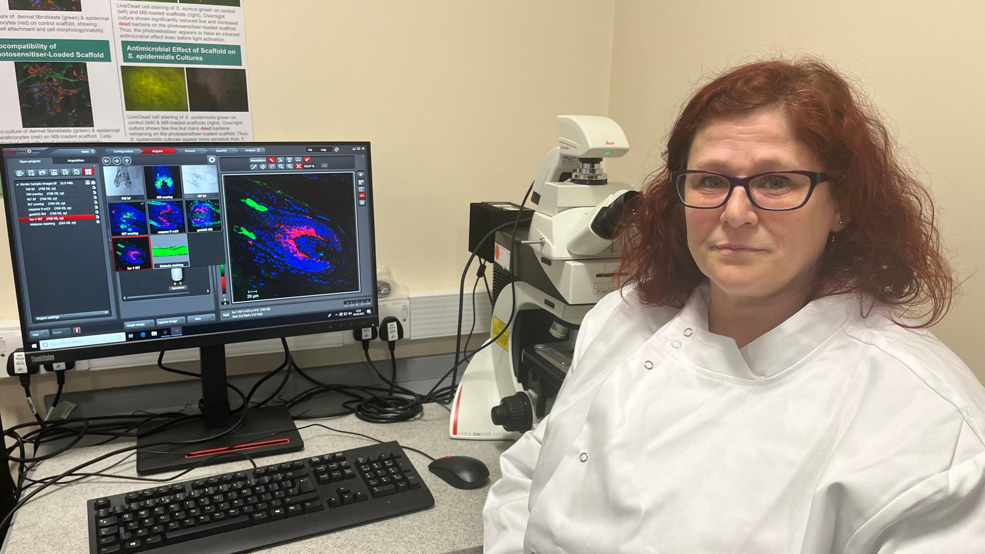 Dr Kirsten Riches-Suman in a lab coat in front of a computer and microscope.