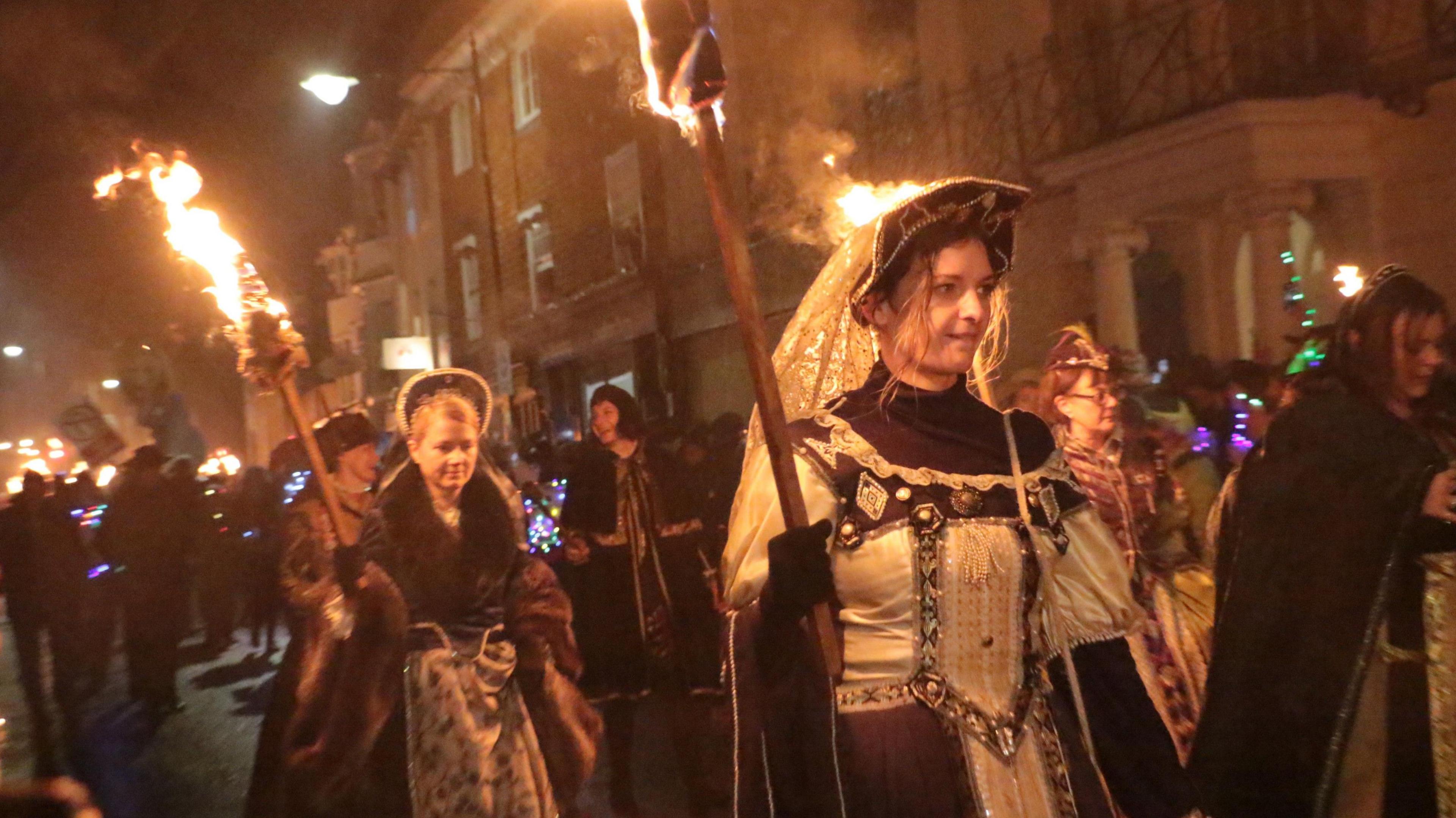 Women dressed in Tudor costumes carrying flaming torches through the streets of Lewes during its annual bonfire event.