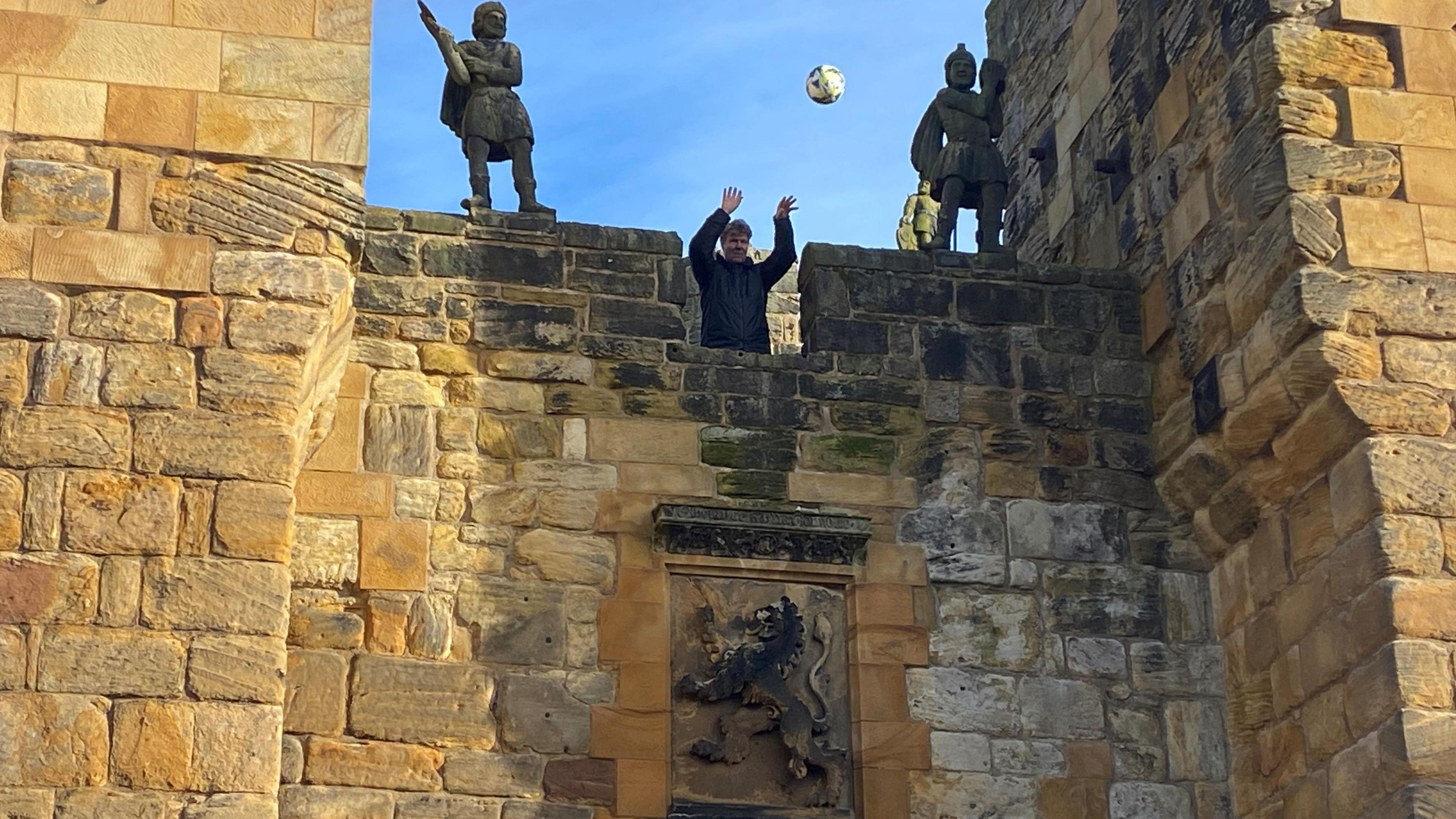 A man dropping a ball from the ramparts of Alnwick Castle.