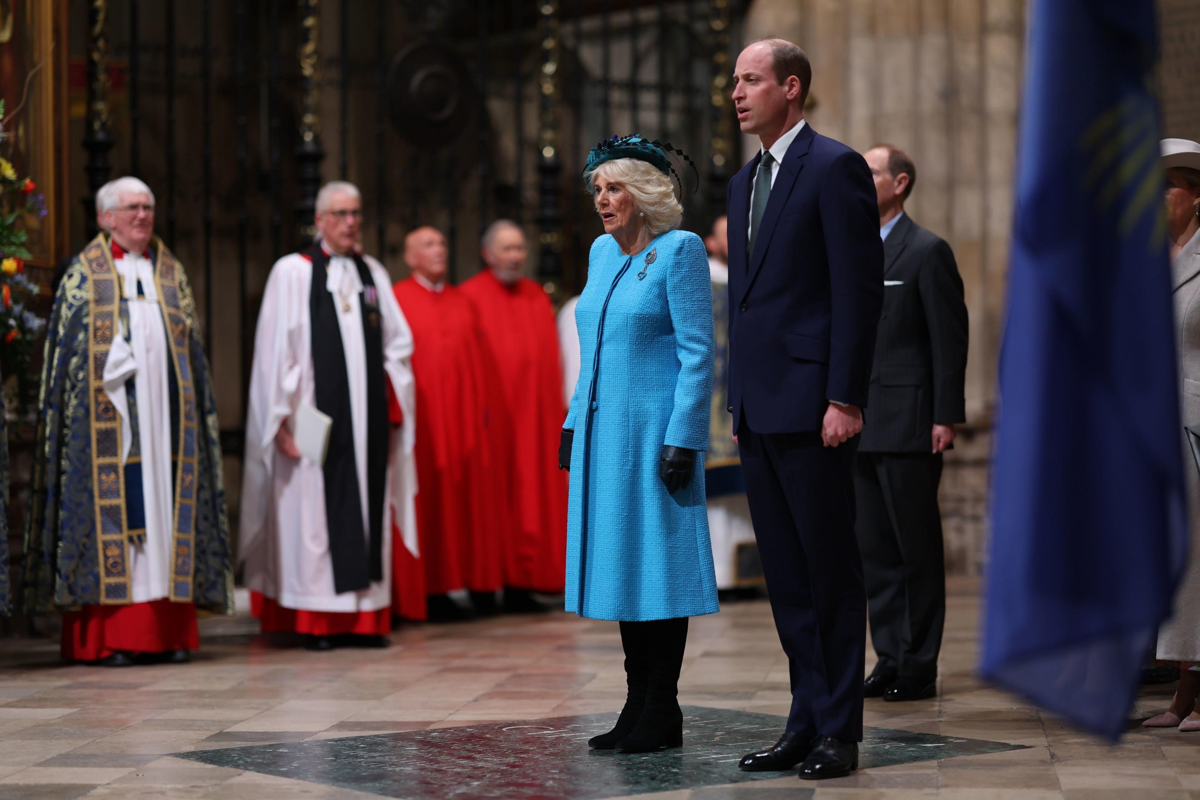 Queens Camilla standing beside Prince William in a suit.