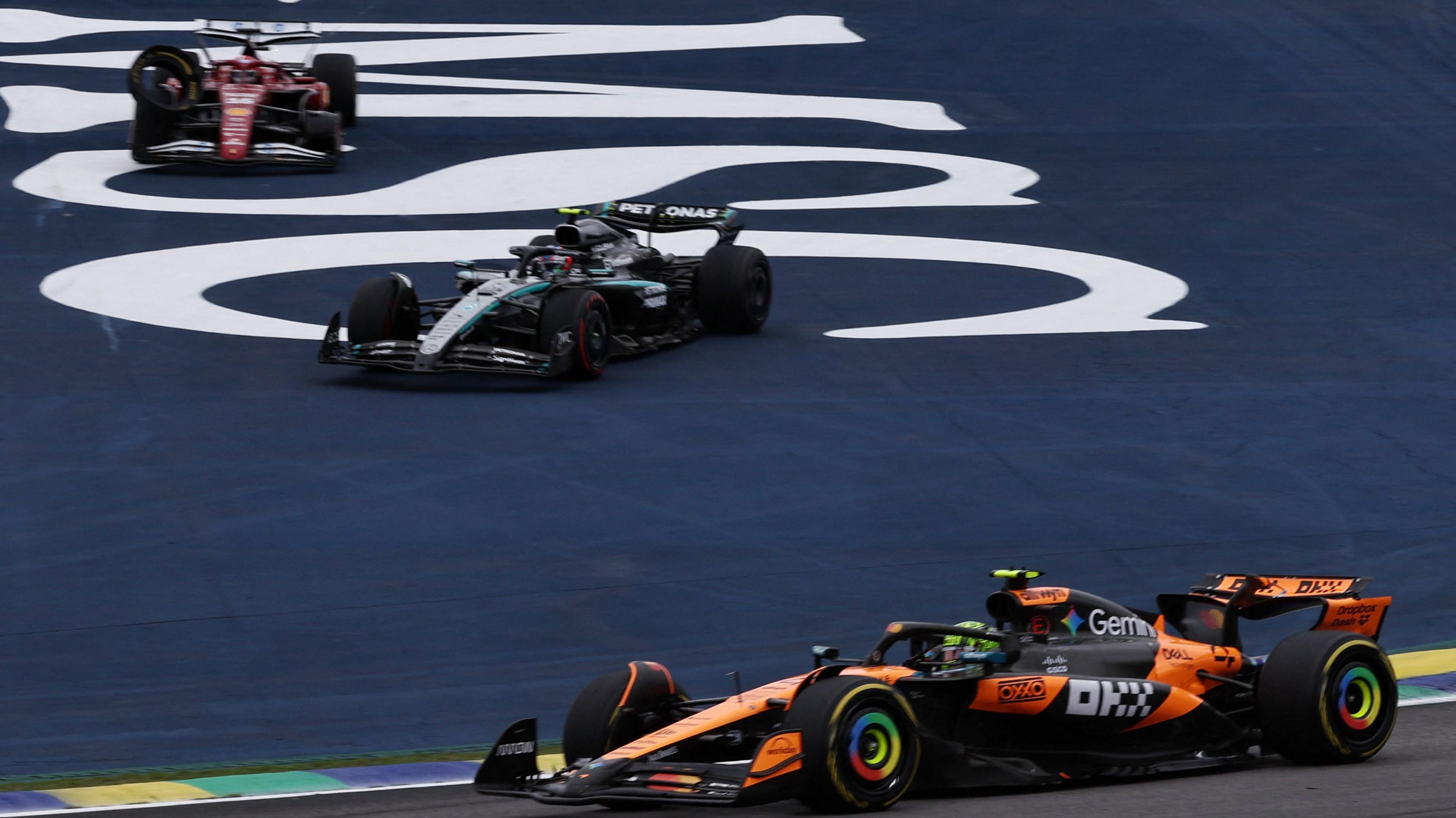 McLaren's Lando Norris leads with Kimi Antonelli's Mercedes and the damaged Ferrari off track after a collision between Oscar Piastri, Antonelli and then Leclerc