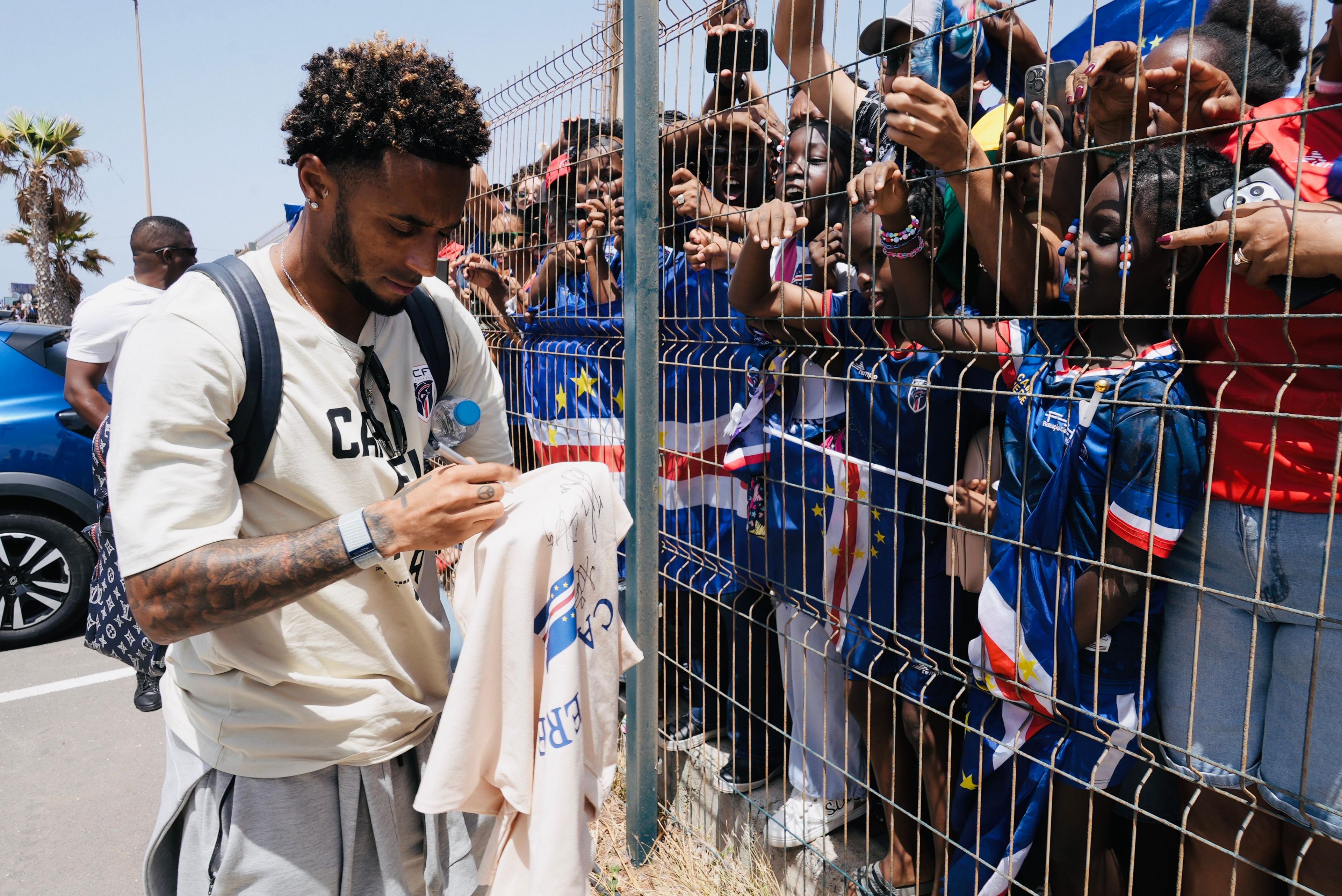 Captain Ryan Mendes signs a white shirt, while separated from fans by a metal fence