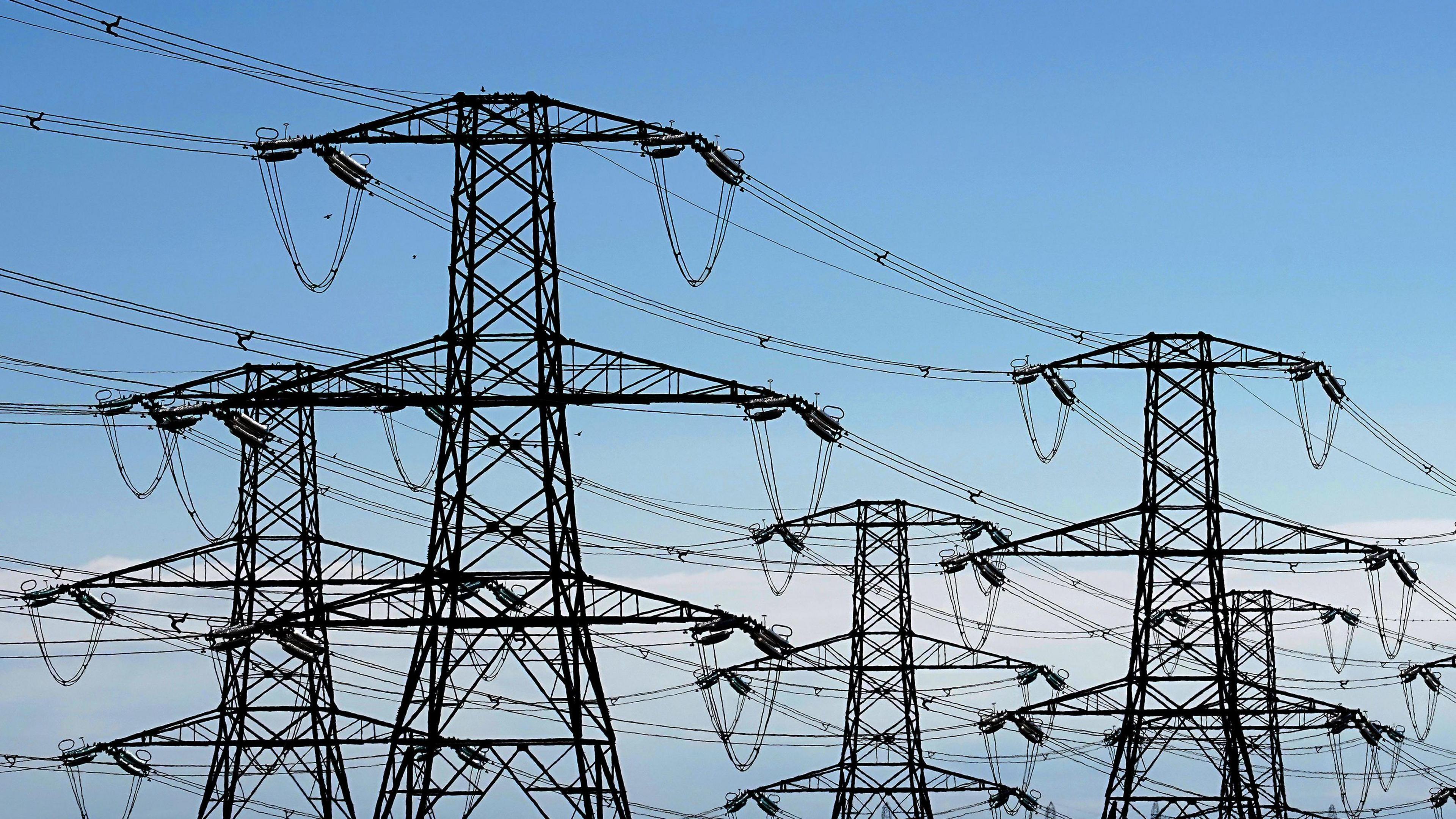 A series of high-voltage pylons against the backdrop of a blue sky