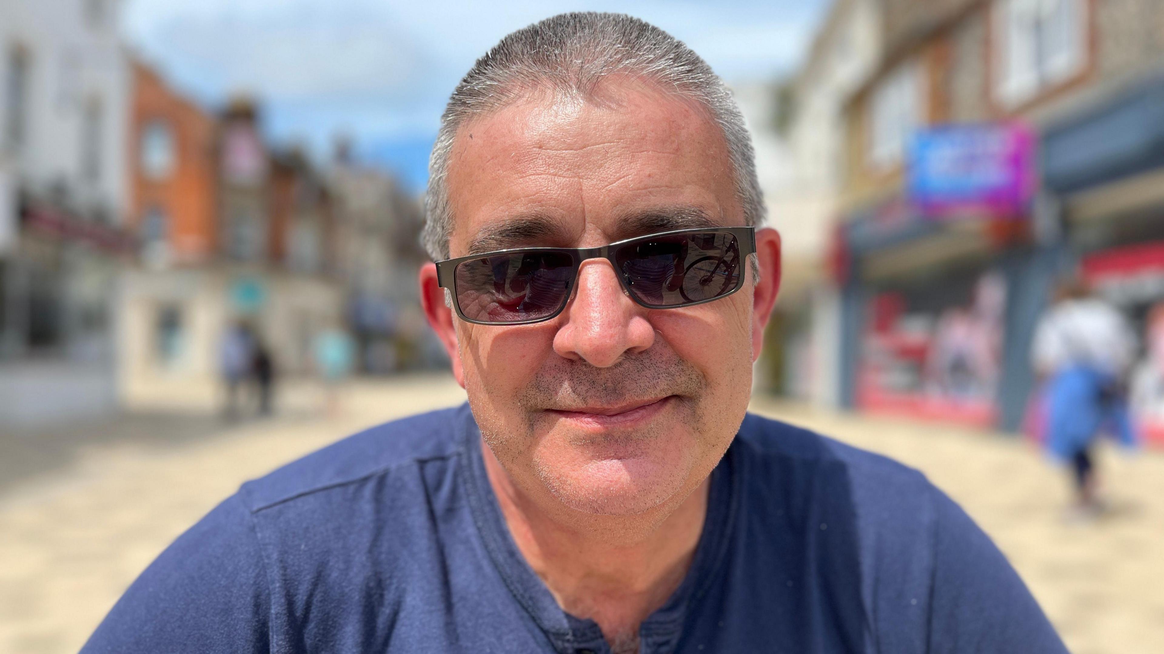 Peter sits in the high street wearing sunglasses