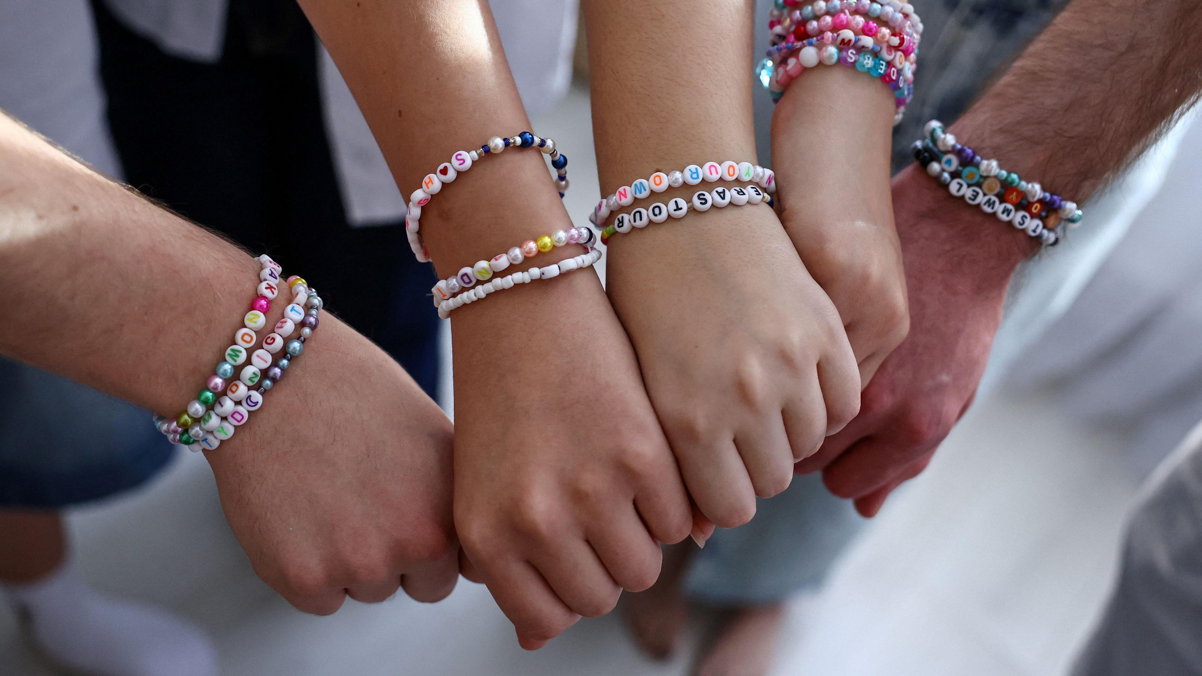 Five hands, each making a fist shape, are held together with bracelets on each of their wrists.