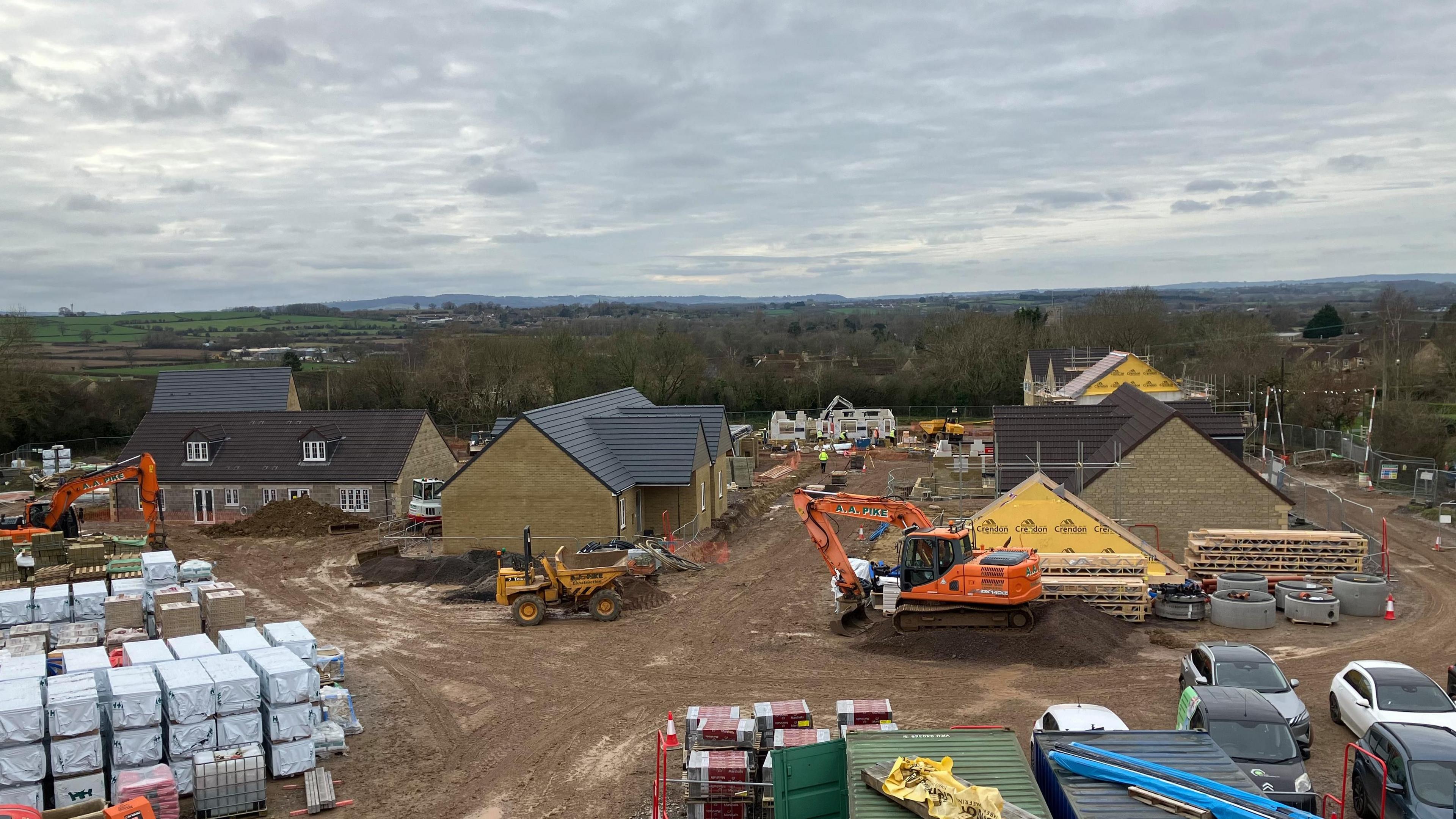 An aerial view of a building site next to countryside and hills in Somerset. Large bags of building materials are visible as well as machinery including an orange digger