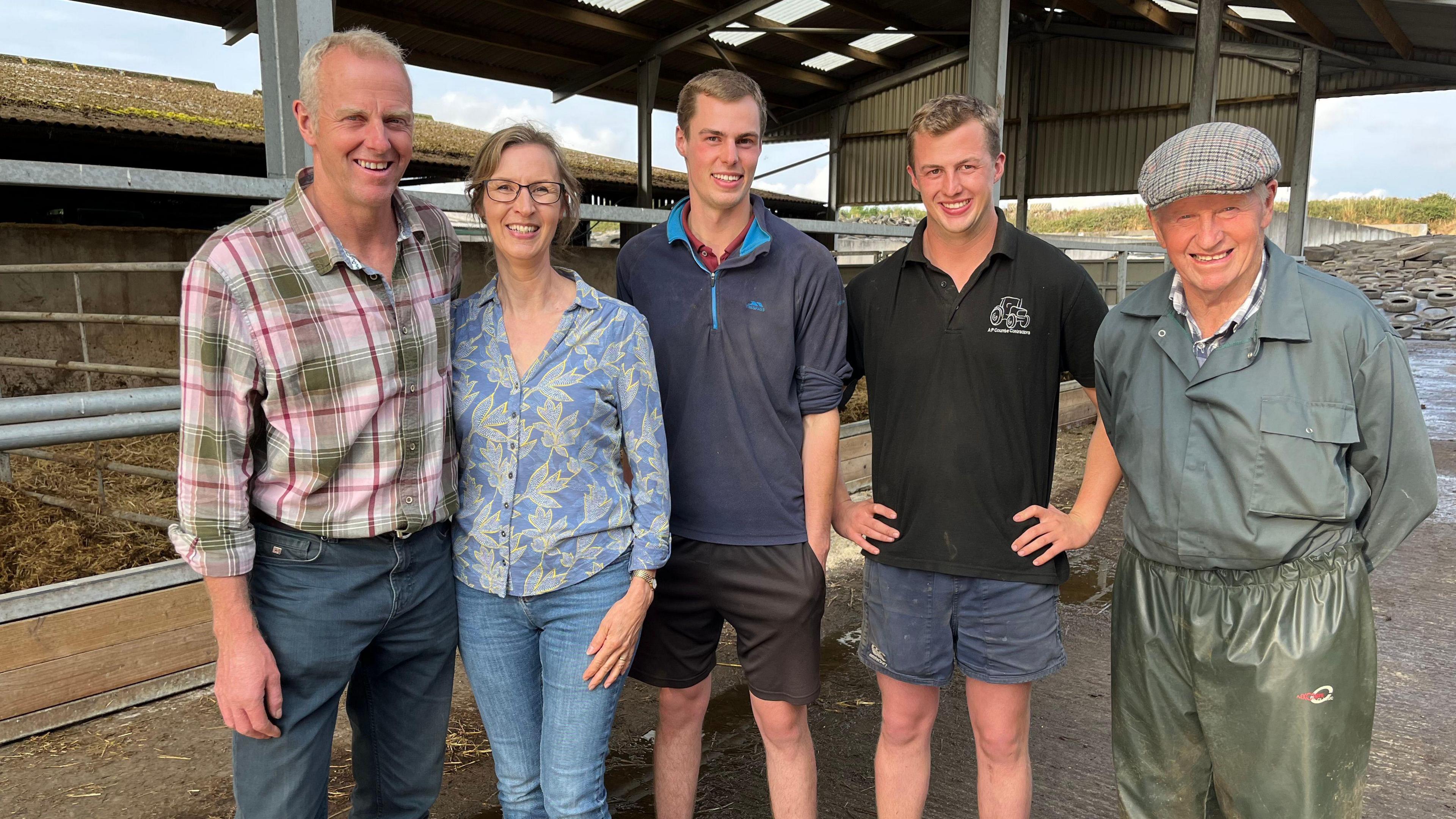 Andrew Jones with wife Jayne, sons Harvey and Oscar and father Roger are standing in a line in a barn. They are all smiling at the camera.