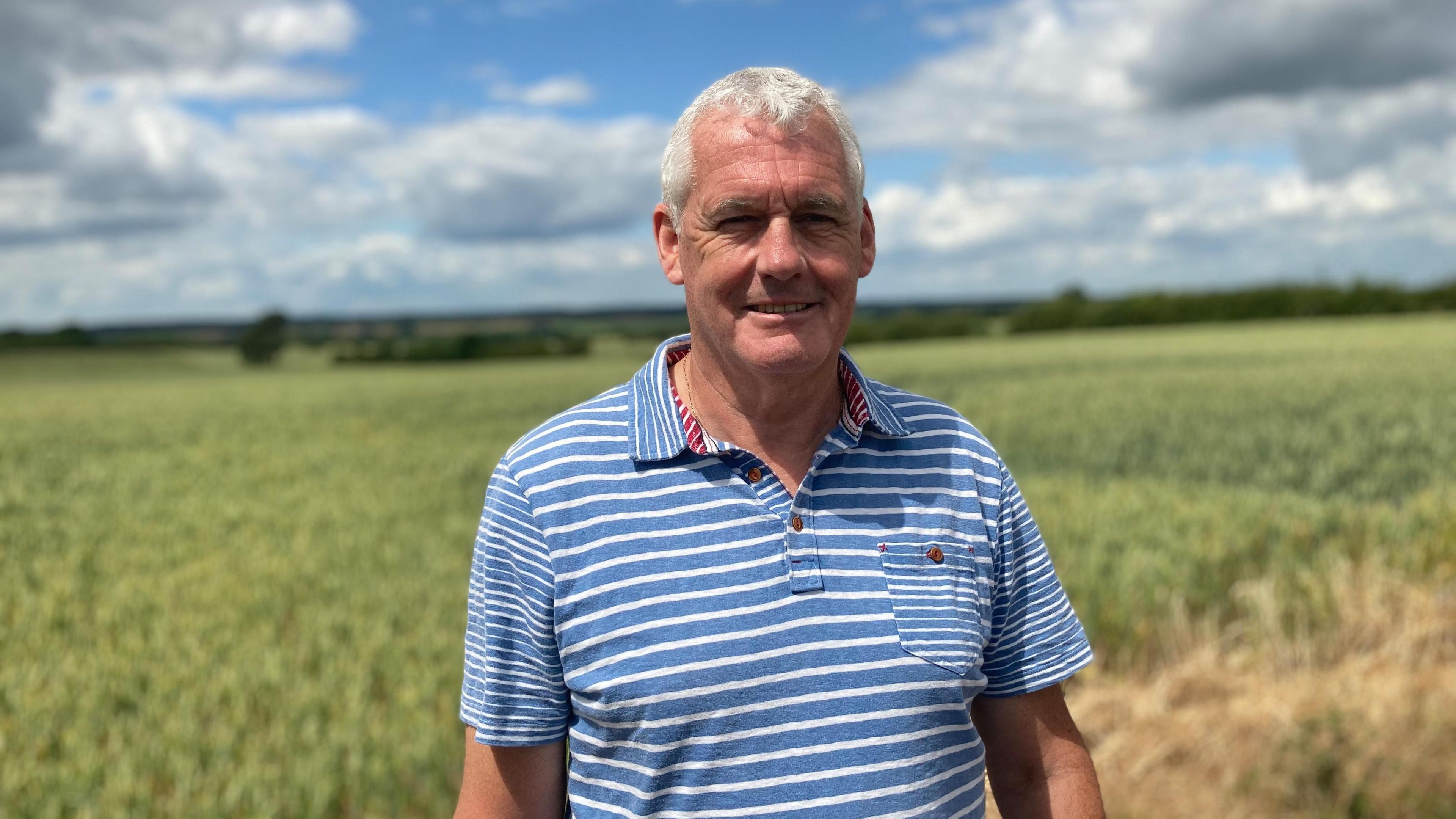 Kevin Shapland, wearing a blue and white striped shirt standing in front of a field.