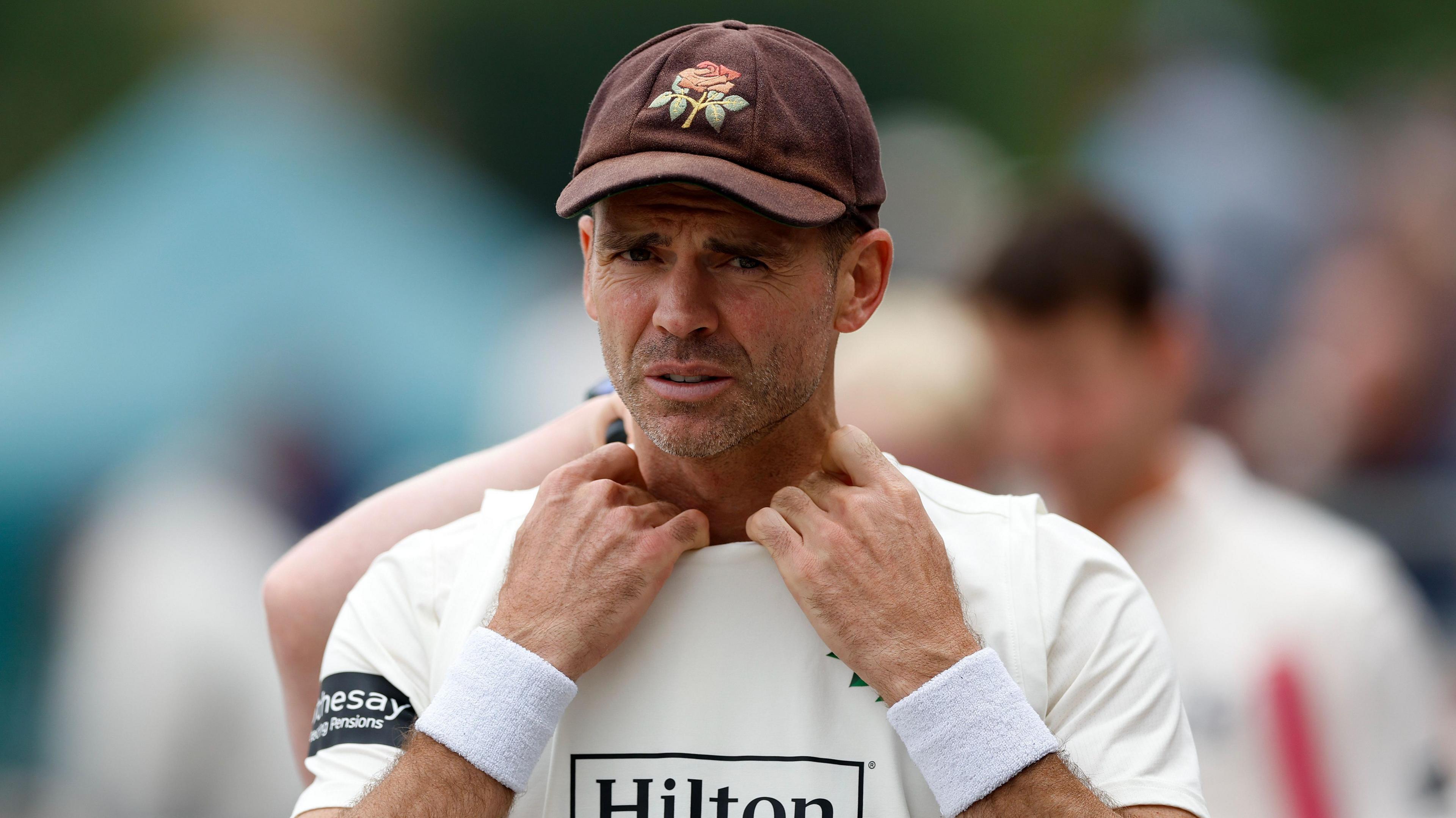 Jimmy Anderson untucks the collar of his shirt from under his sleeveless sweater after an over bowling for Lancashire