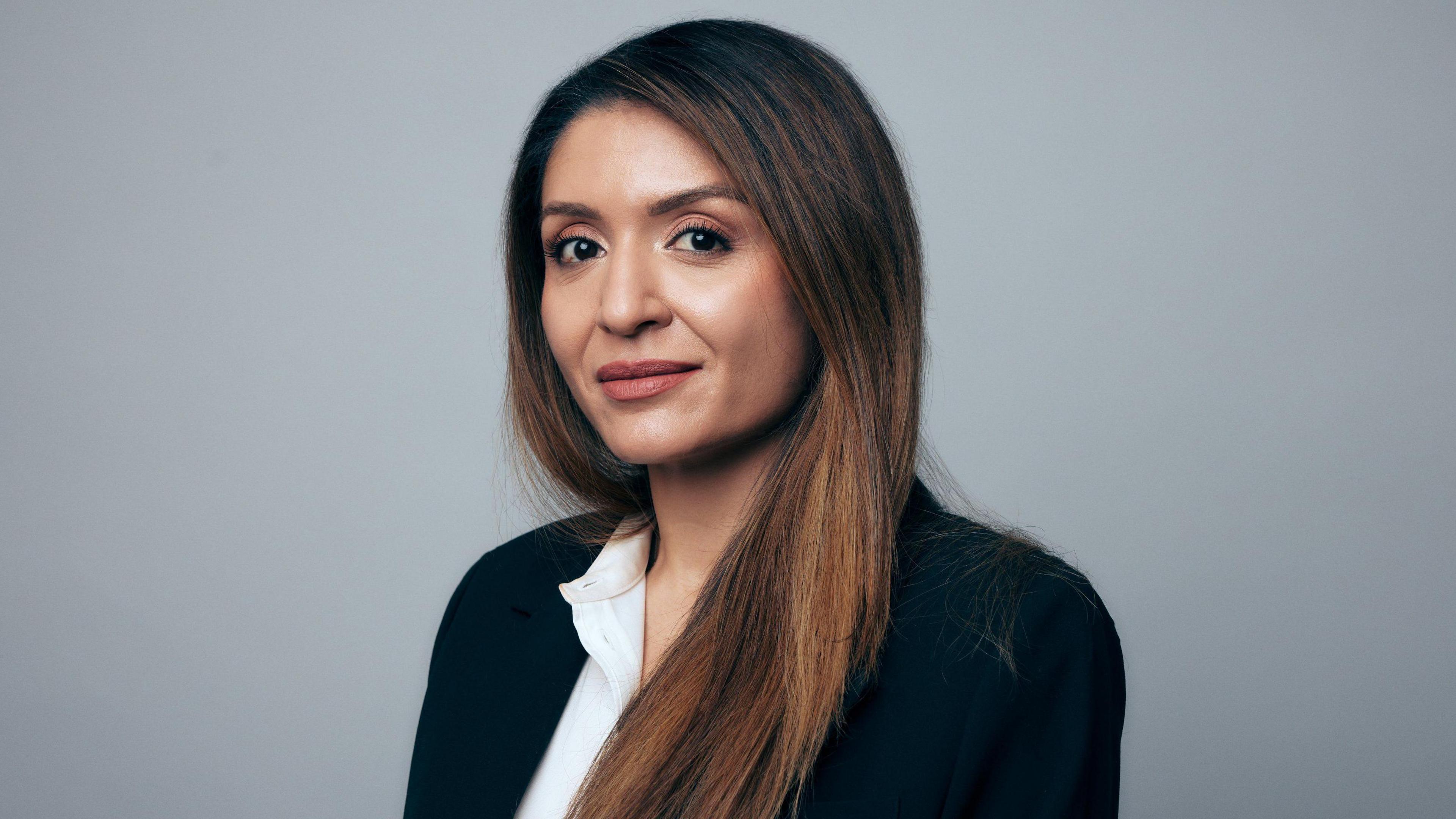 A photo portrait of Shahrzad. She has long brown hair, brown eyes, and wears a dark suit jacket and a white collared shirt.